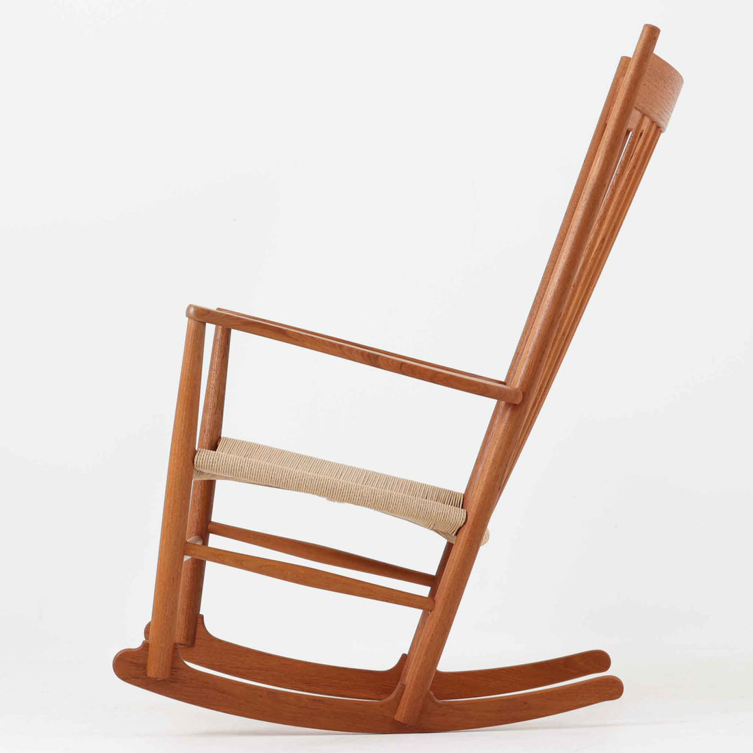 Hans J. Wegner（ハンス・J・ウェグナー）がデザインし、FDB Mobler社が製造したロッキングチェア「J16」。美しいチーク材のフレームとペーパーコードの座面が融合した、北欧ビンテージ家具を代表する一脚です。ハイバックと広めのアームが包み込むような座り心地を生み、ロッキングの揺れが心地よい安らぎをもたらします。経年により深みを増したチーク材の風合いが空間に静かな存在感を添え、読書やリラックスタイムに最適です。チーク材のモデルは希少で、現地デンマークのオークションで入手した確かな逸品です。