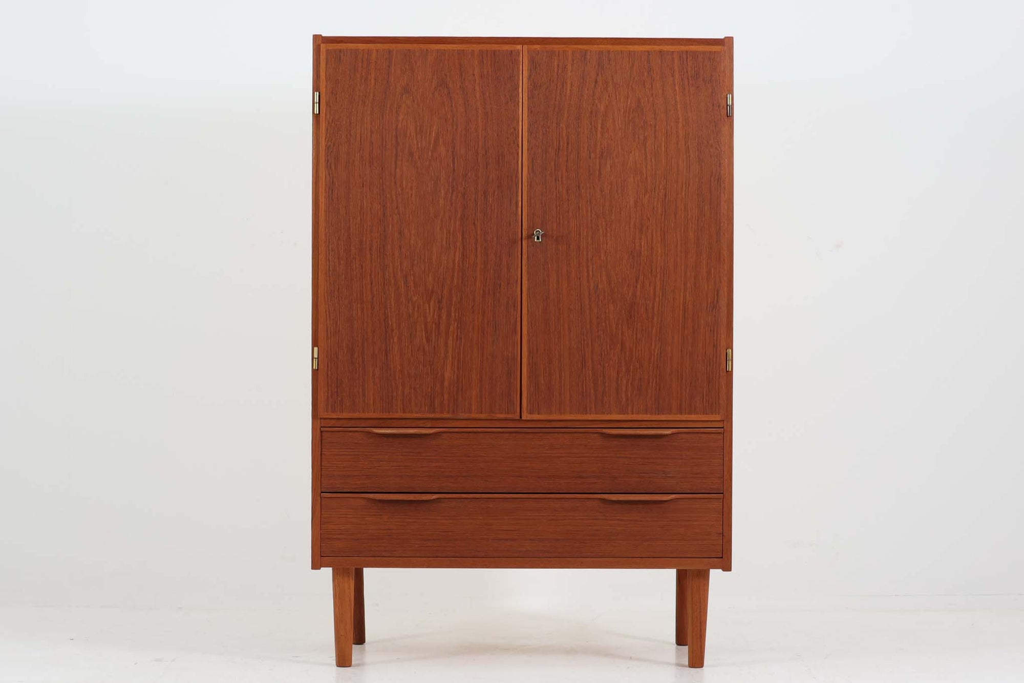 こちらはデンマークより買い付けた収納キャビネットです。上段部分には、北欧家具らしい特徴的なデザインが施されており、鍵を取手として使用しています。大きな開き戸内には高さ調整が可能な棚板が備え付けられており、収納力が高く、使い勝手も良好です。さらに、下段には2つの大きな引き出しがついており、小物や書類などの収納にも便利です。良質なチーク材が使用されており、温かみのある色合いと耐久性を兼ね備えた一品です。北欧らしいシンプルで機能的なデザインが、お部屋をより一層引き立てます。