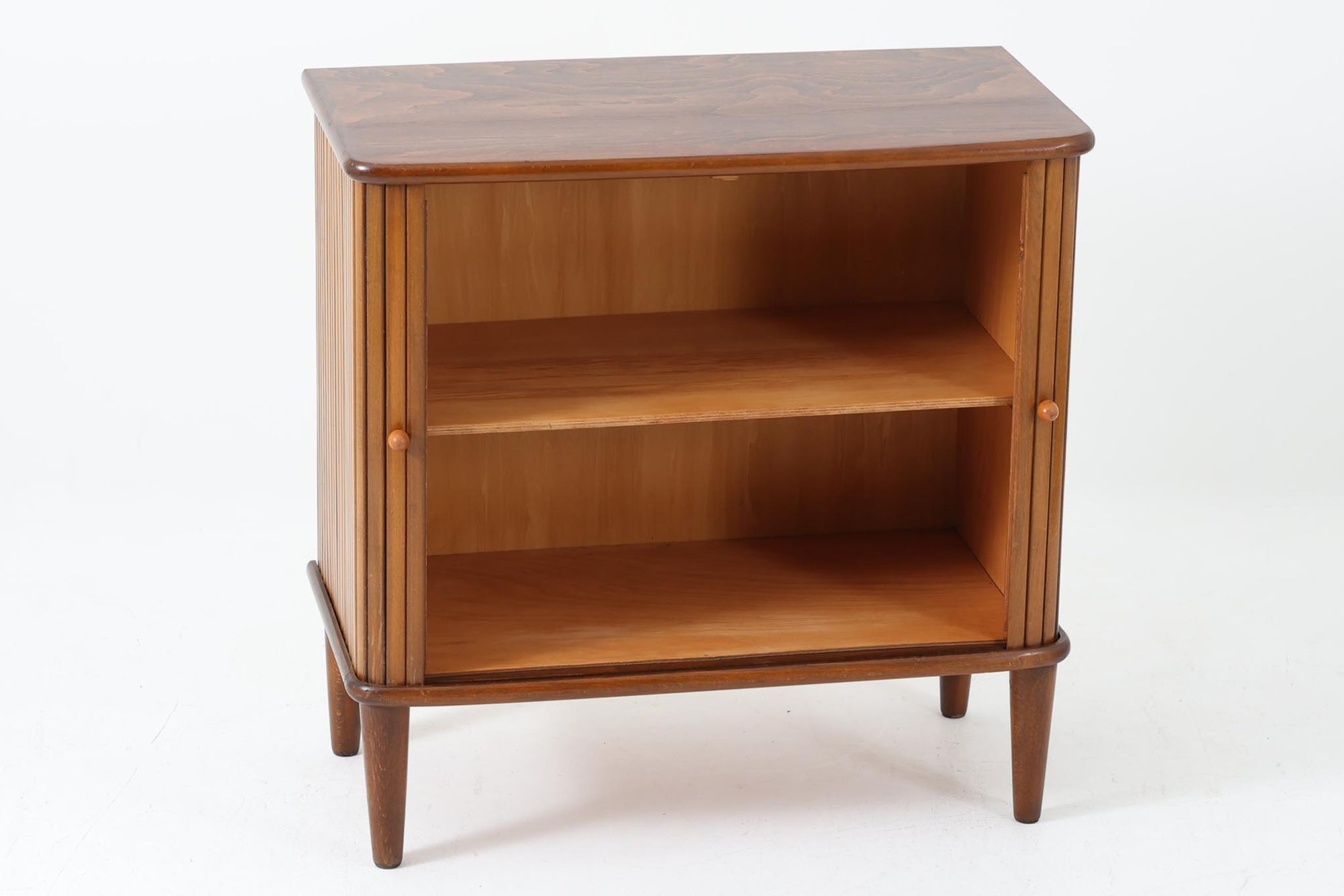 北欧デンマークで製造された、蛇腹扉が特徴的なビンテージキャビネットです。素材にはビーチ材と思われる無垢材や突板が使用されており、ステイン塗装により落ち着いたブラウンカラーに仕上げられています。前面には細かな縦ラインが連続する蛇腹扉が配され、開閉時に滑らかに動く美しい構造が魅力です。内部には棚板が一枚付属しており、収納としての機能性も十分です。丸脚や小さな丸い取っ手も北欧らしい柔らかなディテールで、リビングや玄関、寝室などさまざまな空間に自然に溶け込む一台です。