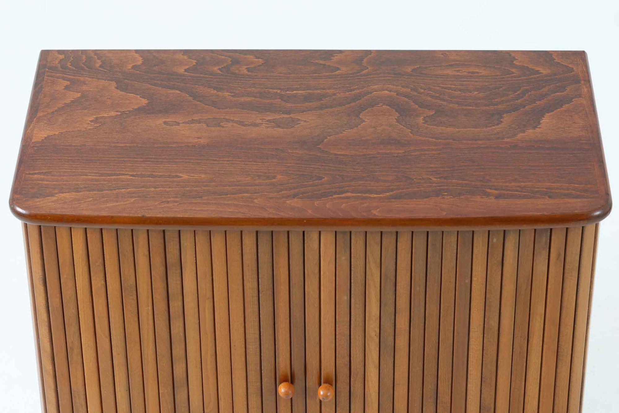 北欧デンマークで製造された、蛇腹扉が特徴的なビンテージキャビネットです。素材にはビーチ材と思われる無垢材や突板が使用されており、ステイン塗装により落ち着いたブラウンカラーに仕上げられています。前面には細かな縦ラインが連続する蛇腹扉が配され、開閉時に滑らかに動く美しい構造が魅力です。内部には棚板が一枚付属しており、収納としての機能性も十分です。丸脚や小さな丸い取っ手も北欧らしい柔らかなディテールで、リビングや玄関、寝室などさまざまな空間に自然に溶け込む一台です。