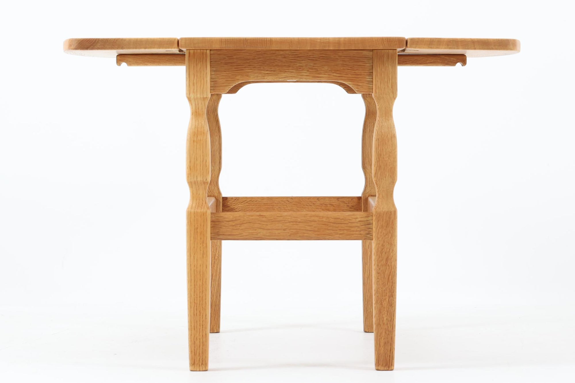 デンマークの建築家Henning Kjaernulf（ヘニング・ケアヌルフ）によってデザインされた、オーク無垢材のドロップリーフ式センターテーブルです。製造は高品質な家具で知られるEGモブラー社。無垢材ならではの美しい木目と、クラシカルで彫刻的な脚部のラインが印象的です。天板は両側に開閉式のリーフが備わっており、来客時や作業時には広げてスペースを拡張できるなど、実用性も兼ね備えています。テーブルの高さはやや高めの設計で、ソファ前に置いても手元が使いやすく、センターテーブルとして快適にお使いいただけます。必要に応じてサイドテーブルやティーテーブルとしても活躍する、用途の広い一台です。