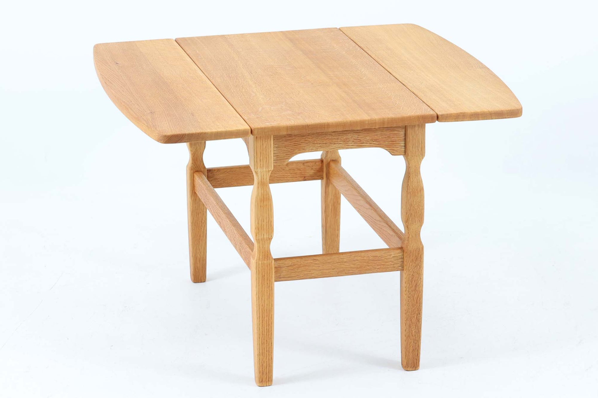 デンマークの建築家Henning Kjaernulf（ヘニング・ケアヌルフ）によってデザインされた、オーク無垢材のドロップリーフ式センターテーブルです。製造は高品質な家具で知られるEGモブラー社。無垢材ならではの美しい木目と、クラシカルで彫刻的な脚部のラインが印象的です。天板は両側に開閉式のリーフが備わっており、来客時や作業時には広げてスペースを拡張できるなど、実用性も兼ね備えています。テーブルの高さはやや高めの設計で、ソファ前に置いても手元が使いやすく、センターテーブルとして快適にお使いいただけます。必要に応じてサイドテーブルやティーテーブルとしても活躍する、用途の広い一台です。