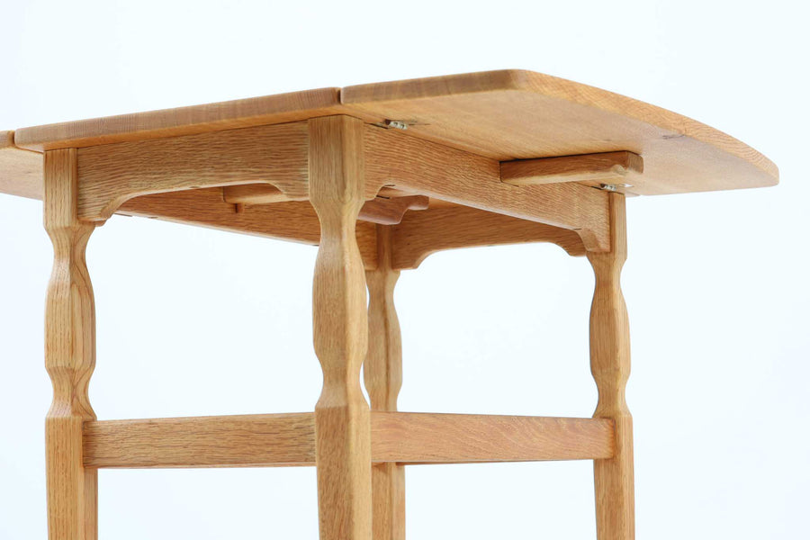 デンマークの建築家Henning Kjaernulf（ヘニング・ケアヌルフ）によってデザインされた、オーク無垢材のドロップリーフ式センターテーブルです。製造は高品質な家具で知られるEGモブラー社。無垢材ならではの美しい木目と、クラシカルで彫刻的な脚部のラインが印象的です。天板は両側に開閉式のリーフが備わっており、来客時や作業時には広げてスペースを拡張できるなど、実用性も兼ね備えています。テーブルの高さはやや高めの設計で、ソファ前に置いても手元が使いやすく、センターテーブルとして快適にお使いいただけます。必要に応じてサイドテーブルやティーテーブルとしても活躍する、用途の広い一台です。