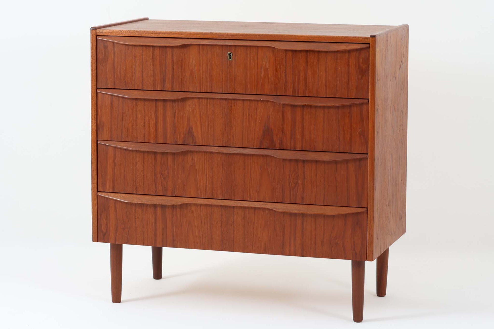 デンマークより買い付けた4段チェストです。良質なチーク材が使用されており、その温かみのある色味と美しい木目が魅力的です。北欧家具らしいシンプルで洗練されたデザインに、バータイプの取手がアクセントとなっています。少し大きめのサイズ感で、収納力も十分で、衣類や小物を整理できる実用的なアイテムです。日々の生活空間に温かみと落ち着きを加える一品としておすすめです。