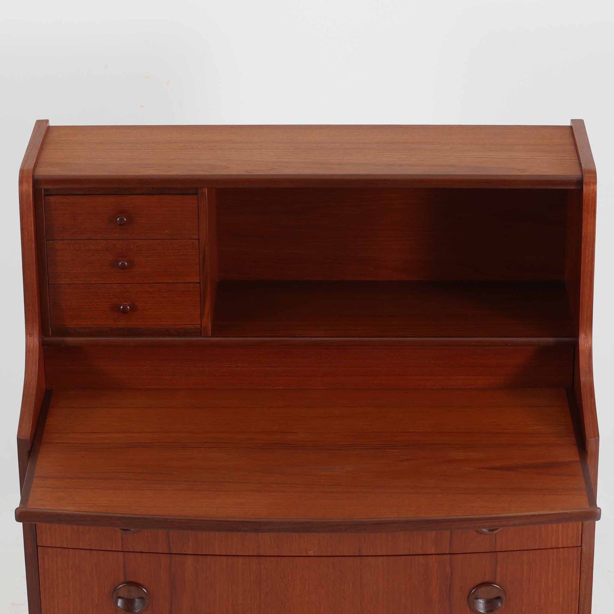 デンマーク製ライティングビューロです。上段には3杯の小引き出しとオープンスペースを備え、文具や手紙などを整理しながら使える実用的な設計です。丸い意匠の取っ手や滑らかな脚部のラインが北欧らしい温かみを感じさせ、チーク材の艶やかな木目が上品な印象を与えます。天板を開くと小さな書斎のような空間が広がり、リビングや寝室でも場所を取らず快適に作業が可能です。下段には3杯の引き出しを配置し、書類やノート類もしっかり収納できます。細身の脚部が軽やかさを添え、省スペースながら十分な収納力を兼ね備えた機能美あふれる一台です。経年によって増した風合いが魅力の、上質な北欧ビンテージ家具です。