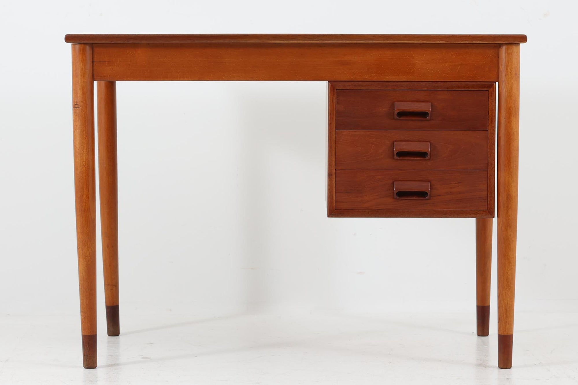 Borge mogensenデザインの小ぶりな片袖デスクは、モーエンセンらしい上質なオーク材が使用された美しいモデルです。デザインの特徴である引き出しの取手も、細部にわたるこだわりが感じられます。本体にはチーク材、脚にはビーチ材が使用され、デンマークの室内靴文化に配慮して、足元には汚れが目立たない濃い色味のチーク材がジョイントされています。洗練されたデザインと実用性を兼ね備えたこのデスクは、どんなインテリアにもマッチするアイテムです。