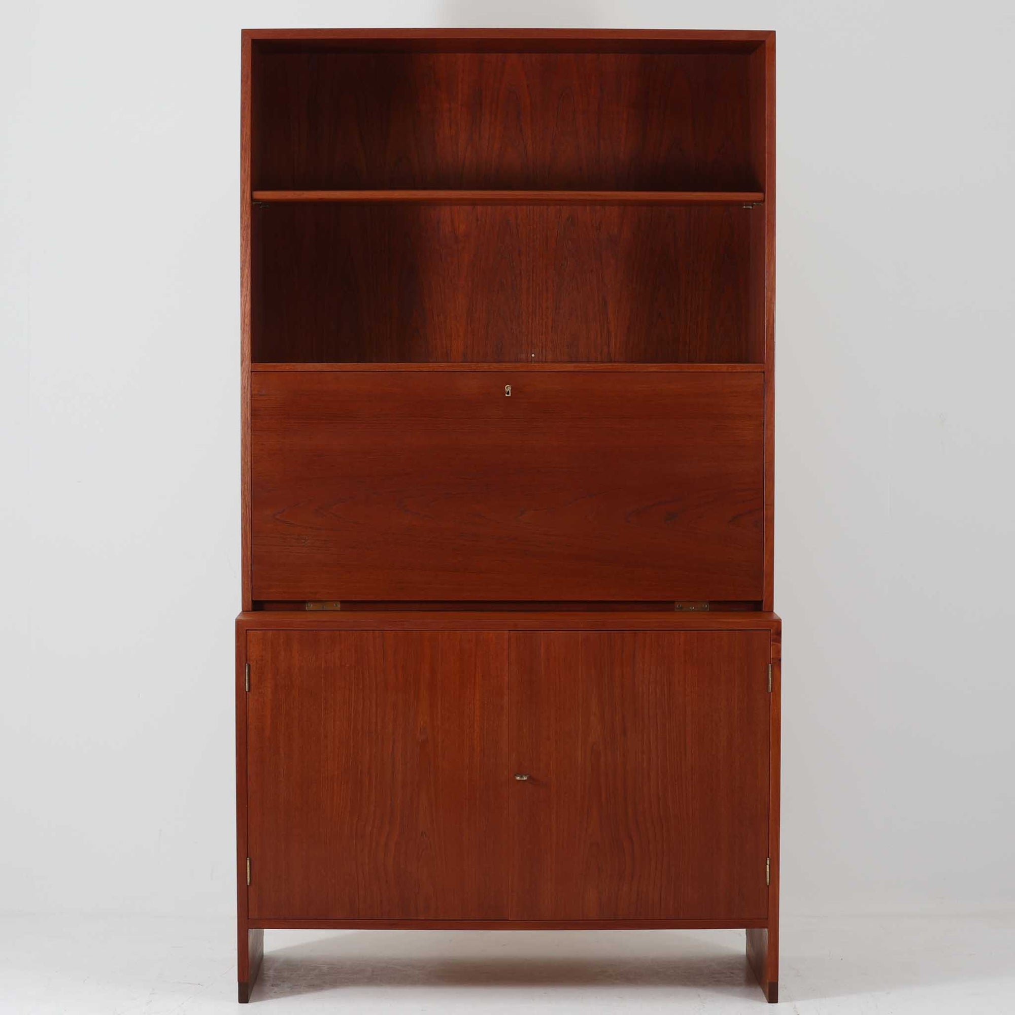 Hans J. Wegnerがデザインし、Ry Mobler社より製造されたこちらのディスプレイシェルフは、チーク材の上質な素材使いと真鍮パーツのディテールが際立つ北欧ビンテージ家具です。シンプルな直線的フォルムの中に、扉付き収納、ドロップダウン式のビューロスペース、小引き出しや仕切り棚など機能的な構造が備わっており、書斎でのデスク兼収納やリビングの飾り棚として多用途に活躍します。年月を経て深みを増した木肌が空間に落ち着いた存在感を与える逸品です。