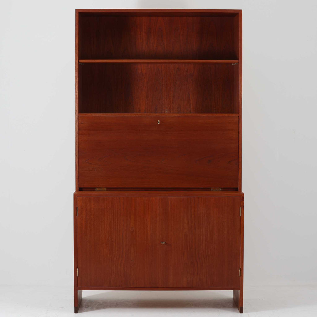 Hans J. Wegnerがデザインし、Ry Mobler社より製造されたこちらのディスプレイシェルフは、チーク材の上質な素材使いと真鍮パーツのディテールが際立つ北欧ビンテージ家具です。シンプルな直線的フォルムの中に、扉付き収納、ドロップダウン式のビューロスペース、小引き出しや仕切り棚など機能的な構造が備わっており、書斎でのデスク兼収納やリビングの飾り棚として多用途に活躍します。年月を経て深みを増した木肌が空間に落ち着いた存在感を与える逸品です。