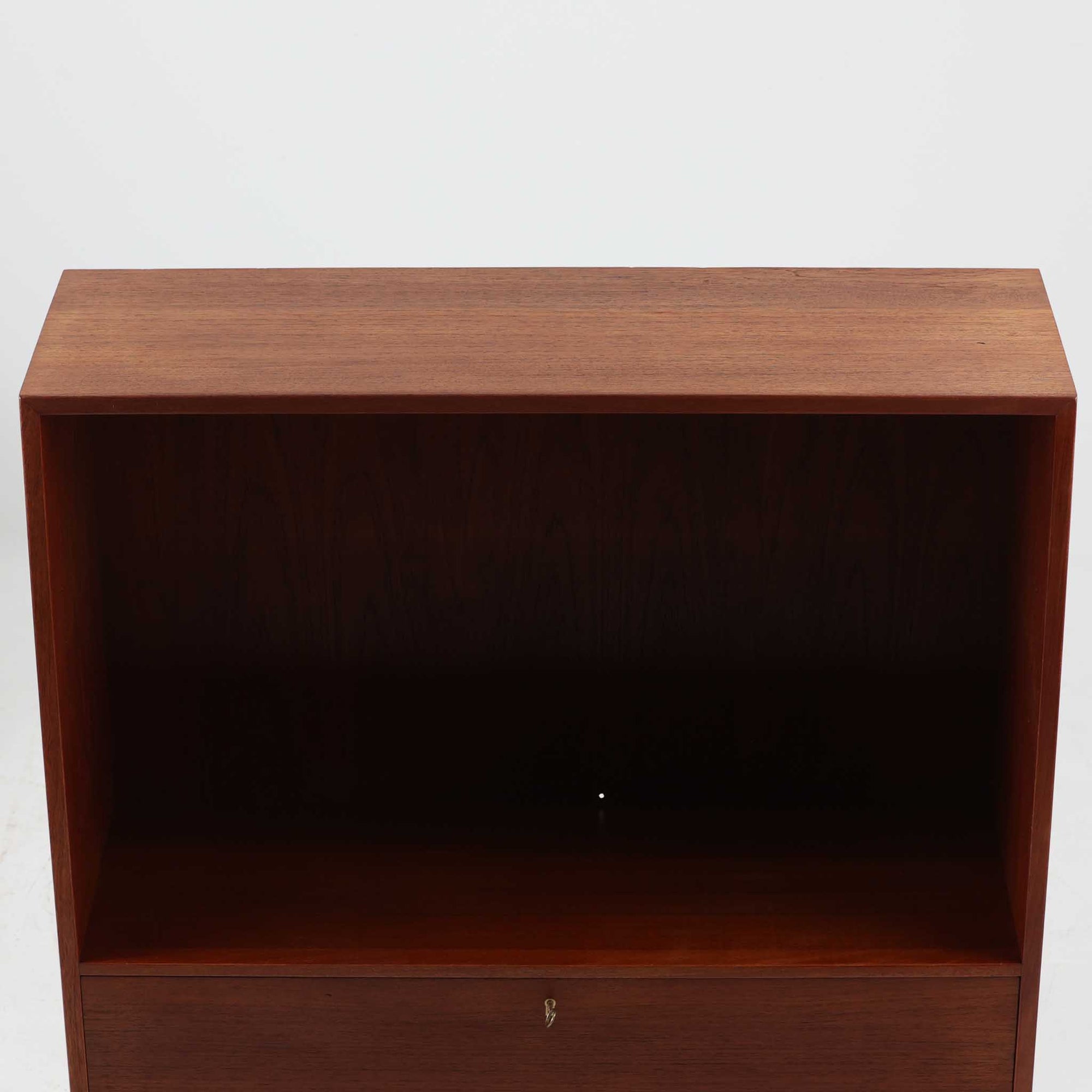 Hans J. Wegnerがデザインし、Ry Mobler社より製造されたこちらのディスプレイシェルフは、チーク材の上質な素材使いと真鍮パーツのディテールが際立つ北欧ビンテージ家具です。シンプルな直線的フォルムの中に、扉付き収納、ドロップダウン式のビューロスペース、小引き出しや仕切り棚など機能的な構造が備わっており、書斎でのデスク兼収納やリビングの飾り棚として多用途に活躍します。年月を経て深みを増した木肌が空間に落ち着いた存在感を与える逸品です。