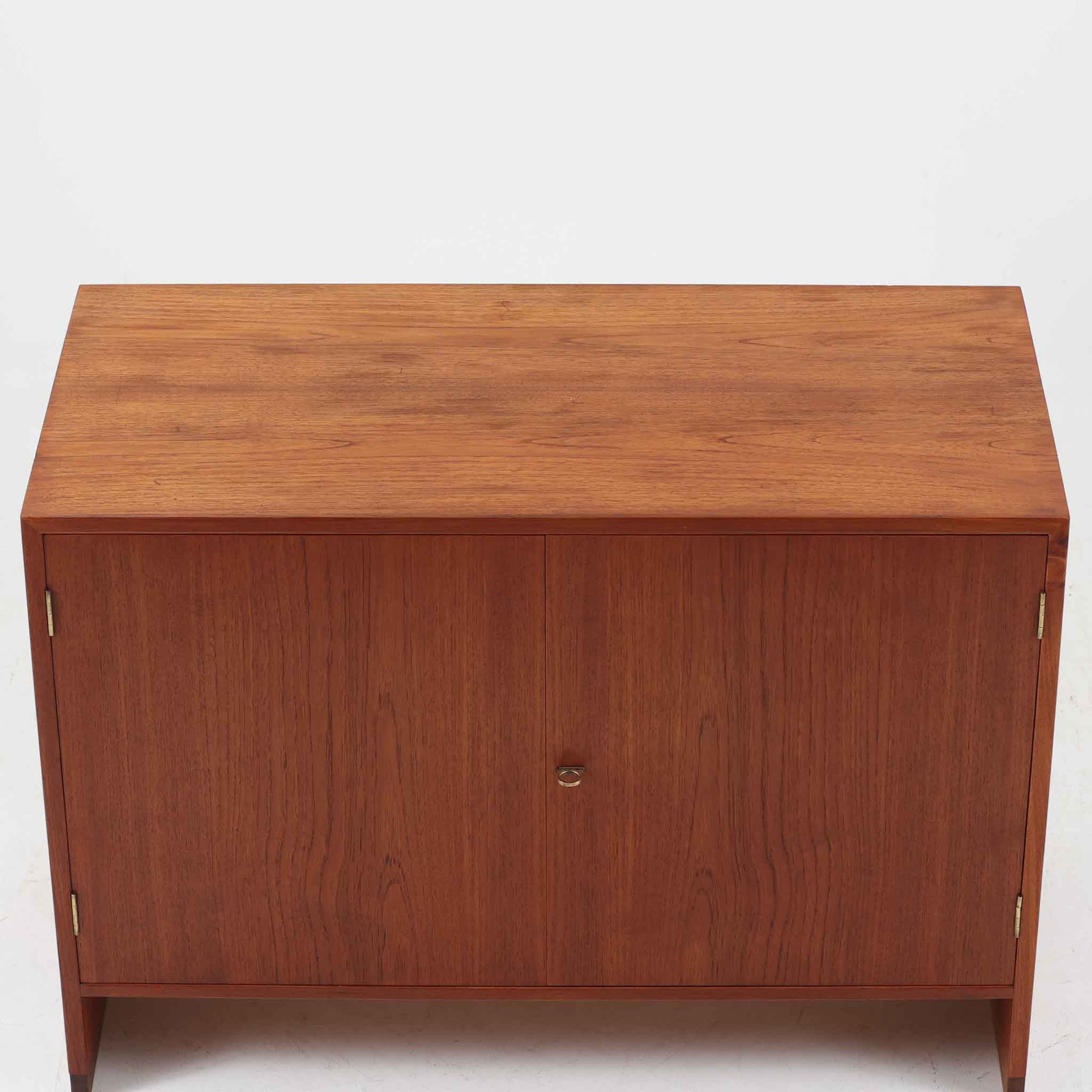 Hans J. Wegnerがデザインし、Ry Mobler社より製造されたこちらのディスプレイシェルフは、チーク材の上質な素材使いと真鍮パーツのディテールが際立つ北欧ビンテージ家具です。シンプルな直線的フォルムの中に、扉付き収納、ドロップダウン式のビューロスペース、小引き出しや仕切り棚など機能的な構造が備わっており、書斎でのデスク兼収納やリビングの飾り棚として多用途に活躍します。年月を経て深みを増した木肌が空間に落ち着いた存在感を与える逸品です。