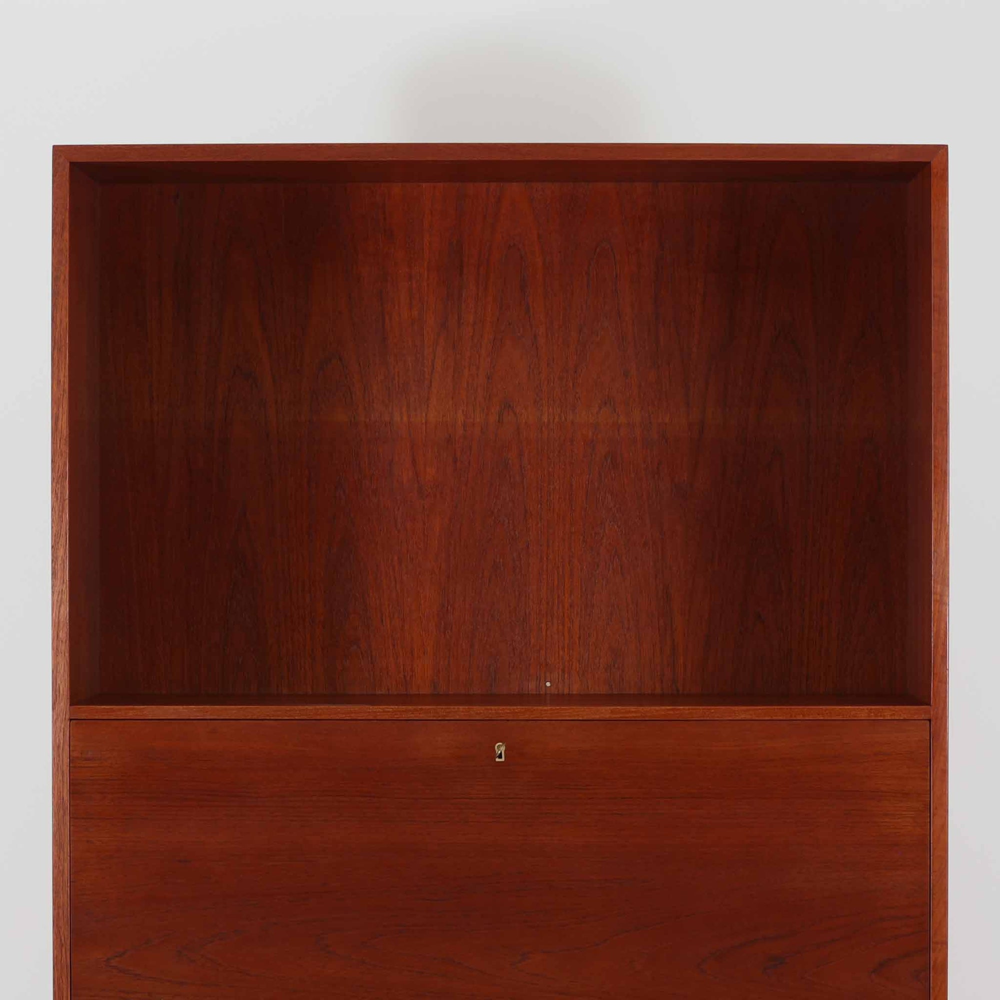 Hans J. Wegnerがデザインし、Ry Mobler社より製造されたこちらのディスプレイシェルフは、チーク材の上質な素材使いと真鍮パーツのディテールが際立つ北欧ビンテージ家具です。シンプルな直線的フォルムの中に、扉付き収納、ドロップダウン式のビューロスペース、小引き出しや仕切り棚など機能的な構造が備わっており、書斎でのデスク兼収納やリビングの飾り棚として多用途に活躍します。年月を経て深みを増した木肌が空間に落ち着いた存在感を与える逸品です。