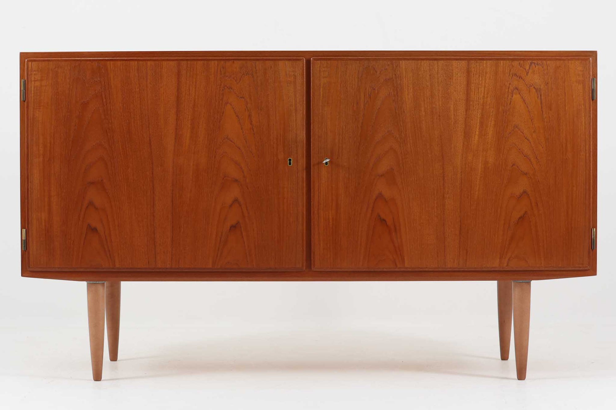 デンマークの家具メーカーHundevad & Co（ハンデバッド）による、Poul Hundevad（ポール・ハンデバッド）デザインのビンテージキャビネットです。美しい木目のチーク材が贅沢に使用され、北欧らしいシンプルで洗練された印象を与えます。両開きの扉内には左側に浅いトレイ状の引き出しが4段、右側には可動棚が2枚設けられており、機能性と収納力に優れた設計。扉の錠前は破損していたため施錠は出来ません。扉の開閉はボールキャッチ方式となっております。鍵は扉開閉用の取っ手として使用します。脚部にはすっきりとしたテーパードレッグが採用され、軽やかで洗練された佇まいが魅力です。リビングやダイニングなど幅広い空間で活躍する一台です。