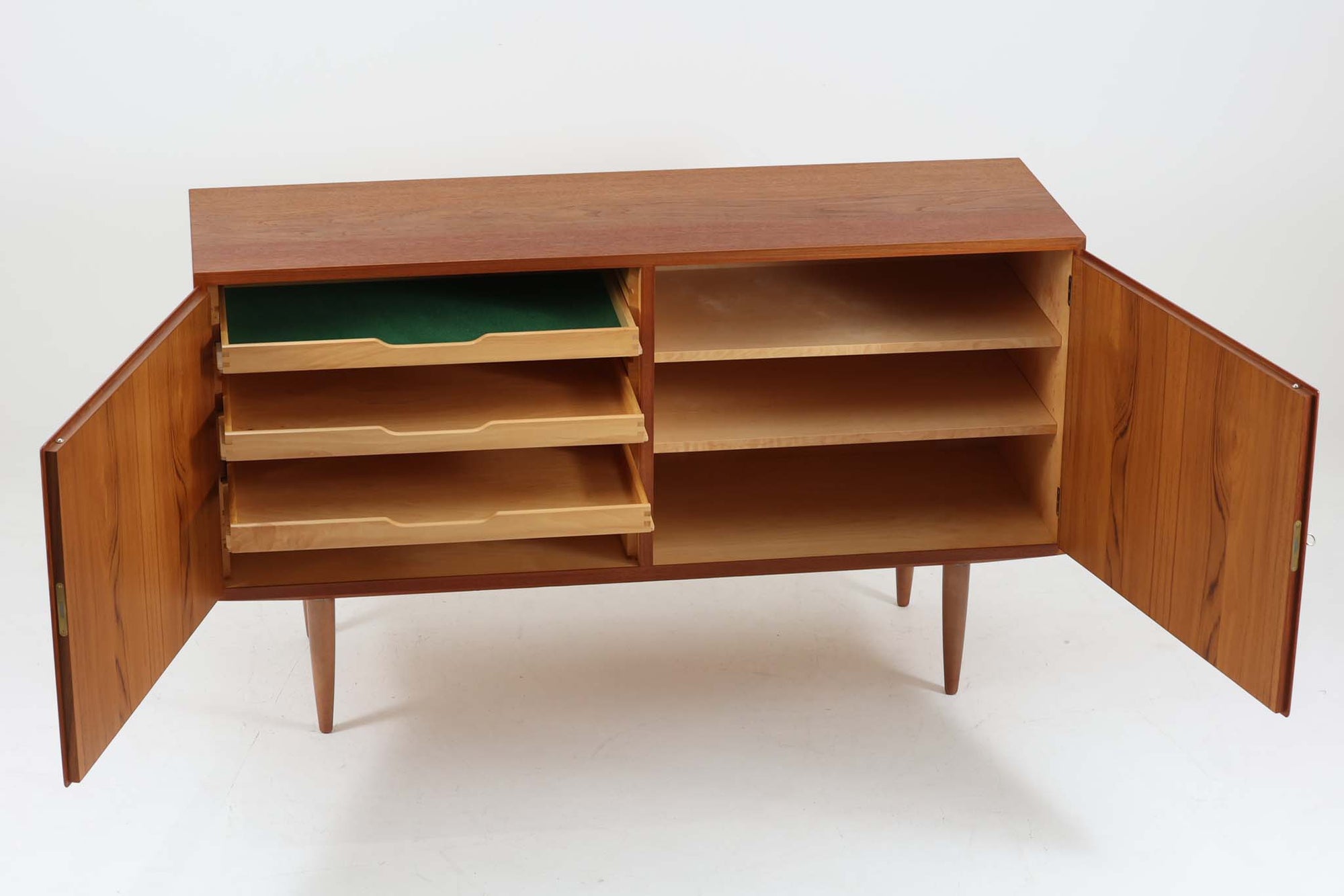 デンマークの家具メーカーHundevad &amp; Co（ハンデバッド）による、Poul Hundevad（ポール・ハンデバッド）デザインのビンテージキャビネットです。美しい木目のチーク材が贅沢に使用され、北欧らしいシンプルで洗練された印象を与えます。両開きの扉内には左側に浅いトレイ状の引き出しが4段、右側には可動棚が2枚設けられており、機能性と収納力に優れた設計。扉の錠前は破損していたため施錠は出来ません。扉の開閉はボールキャッチ方式となっております。鍵は扉開閉用の取っ手として使用します。脚部にはすっきりとしたテーパードレッグが採用され、軽やかで洗練された佇まいが魅力です。リビングやダイニングなど幅広い空間で活躍する一台です。