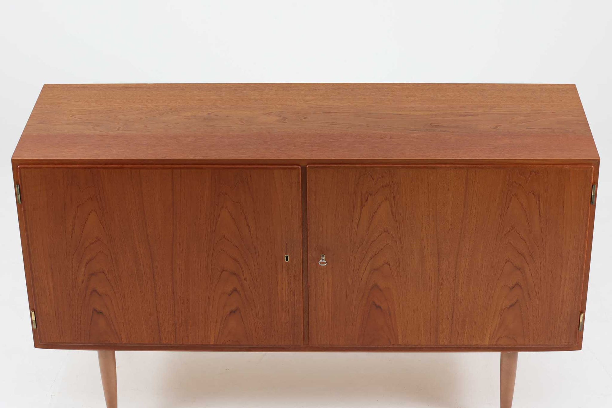 デンマークの家具メーカーHundevad &amp; Co（ハンデバッド）による、Poul Hundevad（ポール・ハンデバッド）デザインのビンテージキャビネットです。美しい木目のチーク材が贅沢に使用され、北欧らしいシンプルで洗練された印象を与えます。両開きの扉内には左側に浅いトレイ状の引き出しが4段、右側には可動棚が2枚設けられており、機能性と収納力に優れた設計。扉の錠前は破損していたため施錠は出来ません。扉の開閉はボールキャッチ方式となっております。鍵は扉開閉用の取っ手として使用します。脚部にはすっきりとしたテーパードレッグが採用され、軽やかで洗練された佇まいが魅力です。リビングやダイニングなど幅広い空間で活躍する一台です。