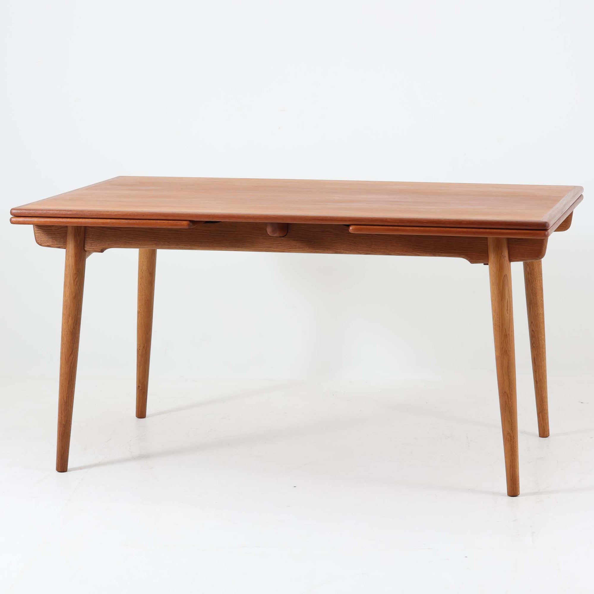 Hans J. Wegnerがデザインを手がけ、Andreas Tuck社から発表されたエクステンションダイニングテーブル「AT312」は、チークとオークのコントラストが美しい北欧ビンテージの名作です。幅140cmから240cmまで拡張可能な機能的な構造により、日常使いから来客時まで柔軟に対応します。緩やかにテーパーした脚部や天板縁の繊細な面取りなど、細部にまでウェグナーの美意識が息づいており、使い込むほどに味わいを深める逸品です。