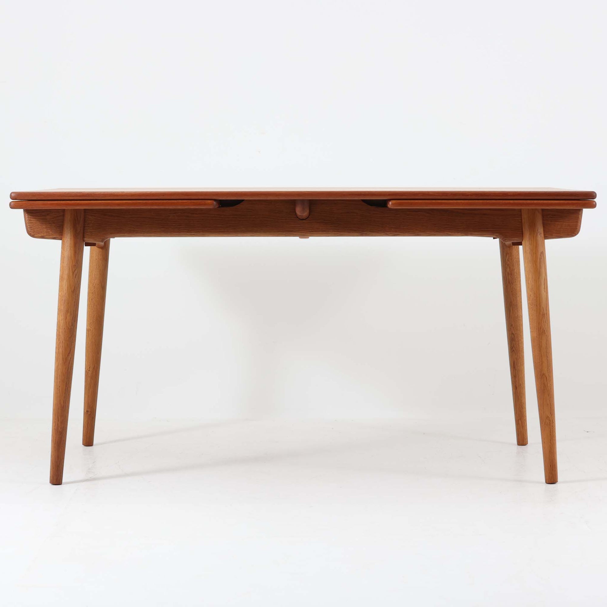 Hans J. Wegnerがデザインを手がけ、Andreas Tuck社から発表されたエクステンションダイニングテーブル「AT312」は、チークとオークのコントラストが美しい北欧ビンテージの名作です。幅140cmから240cmまで拡張可能な機能的な構造により、日常使いから来客時まで柔軟に対応します。緩やかにテーパーした脚部や天板縁の繊細な面取りなど、細部にまでウェグナーの美意識が息づいており、使い込むほどに味わいを深める逸品です。