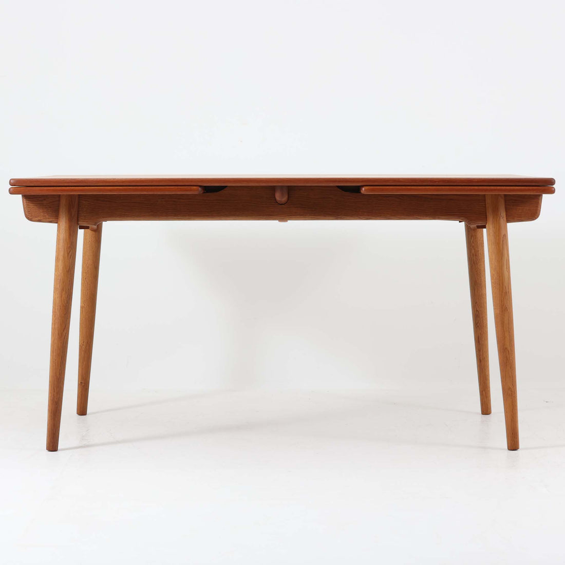 Hans J. Wegnerがデザインを手がけ、Andreas Tuck社から発表されたエクステンションダイニングテーブル「AT312」は、チークとオークのコントラストが美しい北欧ビンテージの名作です。幅140cmから240cmまで拡張可能な機能的な構造により、日常使いから来客時まで柔軟に対応します。緩やかにテーパーした脚部や天板縁の繊細な面取りなど、細部にまでウェグナーの美意識が息づいており、使い込むほどに味わいを深める逸品です。