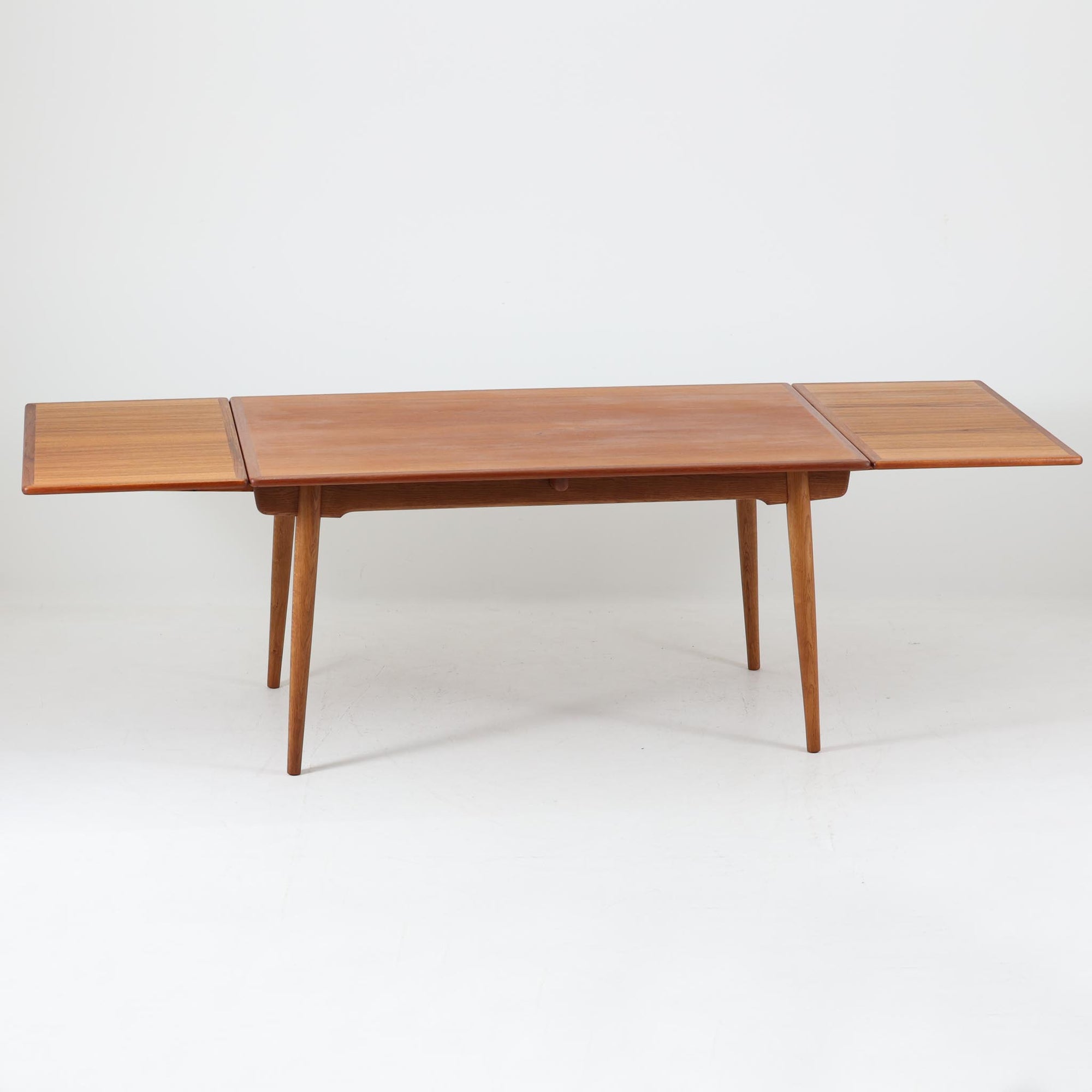 Hans J. Wegnerがデザインを手がけ、Andreas Tuck社から発表されたエクステンションダイニングテーブル「AT312」は、チークとオークのコントラストが美しい北欧ビンテージの名作です。幅140cmから240cmまで拡張可能な機能的な構造により、日常使いから来客時まで柔軟に対応します。緩やかにテーパーした脚部や天板縁の繊細な面取りなど、細部にまでウェグナーの美意識が息づいており、使い込むほどに味わいを深める逸品です。