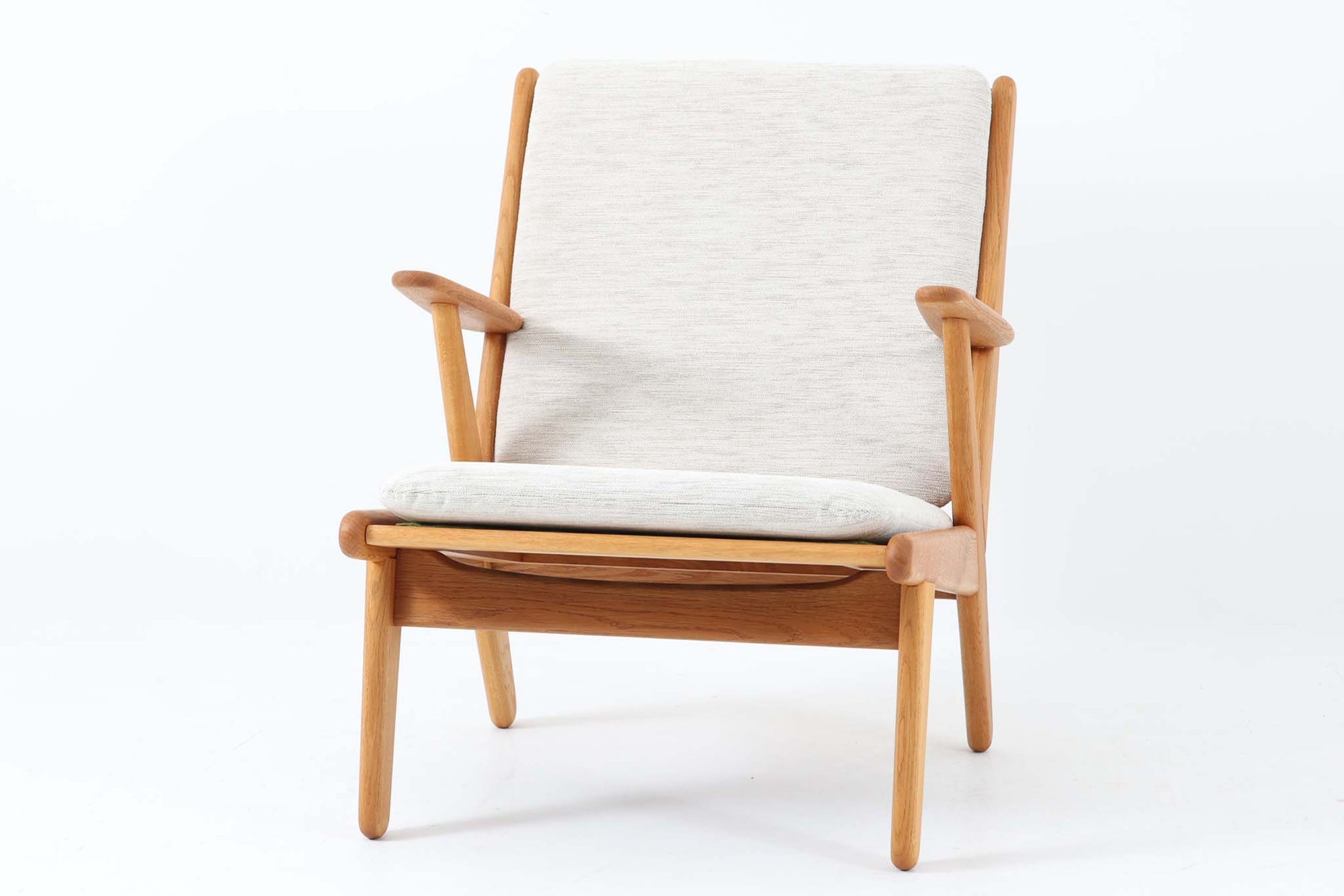 デンマークの国民的ブランドFDBによるビンテージのイージーチェア「J53」。デザイナーは北欧モダンデザインの旗手、Poul m. Volther（ポール・m・ヴォルター）。J53は同氏が手掛けたJシリーズの中でも希少なラウンジチェアタイプで、ゆったりとした座り心地とシンプルな構造美が魅力です。フレームには美しい木目を持つオーク材が使用されており、ナチュラルな風合いが北欧らしい温もりを感じさせます。背面の縦格子デザインや、柔らかくカーブしたアームの形状にも同氏ならではのディテールが感じられます。クッションは新たに張り替え済みで、清潔感のあるアイボリー系のファブリックが品のある印象を与えます。背面に「mADE IN DENmARK」およびFDBの刻印あり。