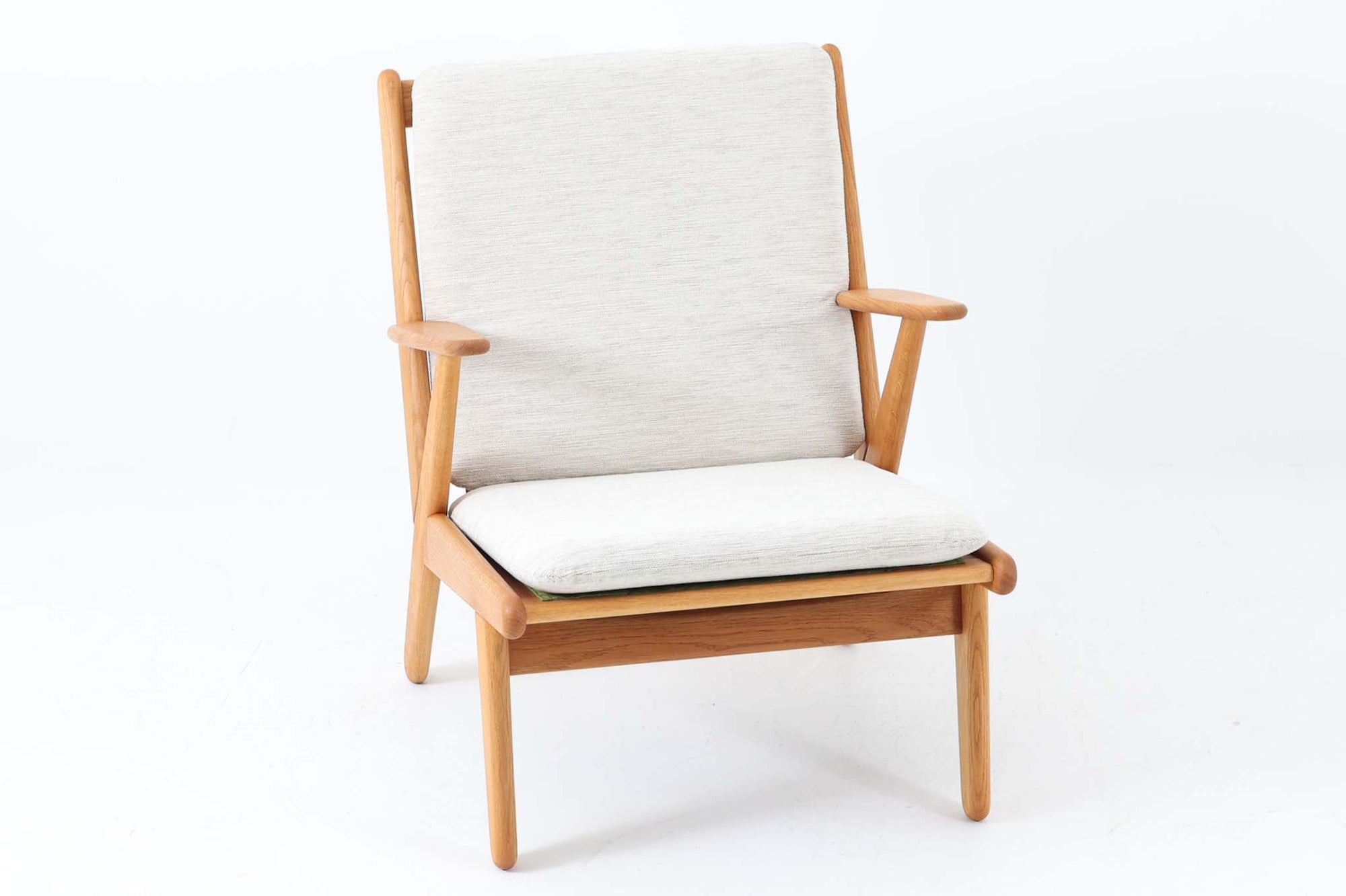 デンマークの国民的ブランドFDBによるビンテージのイージーチェア「J53」。デザイナーは北欧モダンデザインの旗手、Poul m. Volther（ポール・m・ヴォルター）。J53は同氏が手掛けたJシリーズの中でも希少なラウンジチェアタイプで、ゆったりとした座り心地とシンプルな構造美が魅力です。フレームには美しい木目を持つオーク材が使用されており、ナチュラルな風合いが北欧らしい温もりを感じさせます。背面の縦格子デザインや、柔らかくカーブしたアームの形状にも同氏ならではのディテールが感じられます。クッションは新たに張り替え済みで、清潔感のあるアイボリー系のファブリックが品のある印象を与えます。背面に「mADE IN DENmARK」およびFDBの刻印あり。