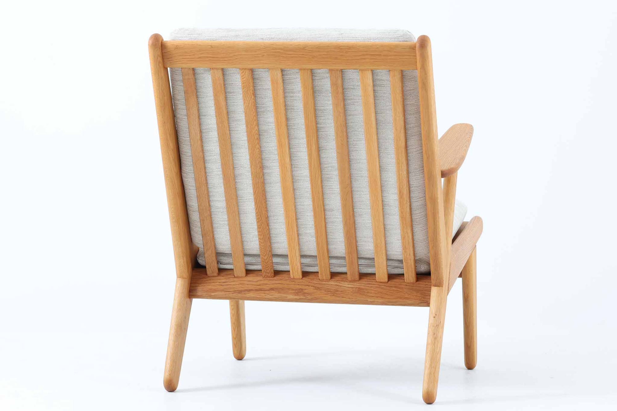 デンマークの国民的ブランドFDBによるビンテージのイージーチェア「J53」。デザイナーは北欧モダンデザインの旗手、Poul m. Volther（ポール・m・ヴォルター）。J53は同氏が手掛けたJシリーズの中でも希少なラウンジチェアタイプで、ゆったりとした座り心地とシンプルな構造美が魅力です。フレームには美しい木目を持つオーク材が使用されており、ナチュラルな風合いが北欧らしい温もりを感じさせます。背面の縦格子デザインや、柔らかくカーブしたアームの形状にも同氏ならではのディテールが感じられます。クッションは新たに張り替え済みで、清潔感のあるアイボリー系のファブリックが品のある印象を与えます。背面に「mADE IN DENmARK」およびFDBの刻印あり。