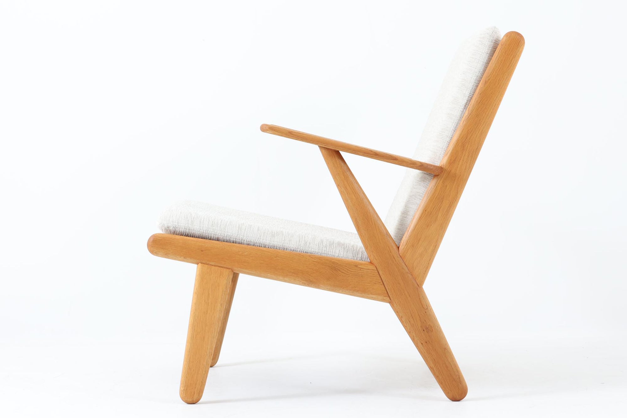 デンマークの国民的ブランドFDBによるビンテージのイージーチェア「J53」。デザイナーは北欧モダンデザインの旗手、Poul m. Volther（ポール・m・ヴォルター）。J53は同氏が手掛けたJシリーズの中でも希少なラウンジチェアタイプで、ゆったりとした座り心地とシンプルな構造美が魅力です。フレームには美しい木目を持つオーク材が使用されており、ナチュラルな風合いが北欧らしい温もりを感じさせます。背面の縦格子デザインや、柔らかくカーブしたアームの形状にも同氏ならではのディテールが感じられます。クッションは新たに張り替え済みで、清潔感のあるアイボリー系のファブリックが品のある印象を与えます。背面に「mADE IN DENmARK」およびFDBの刻印あり。