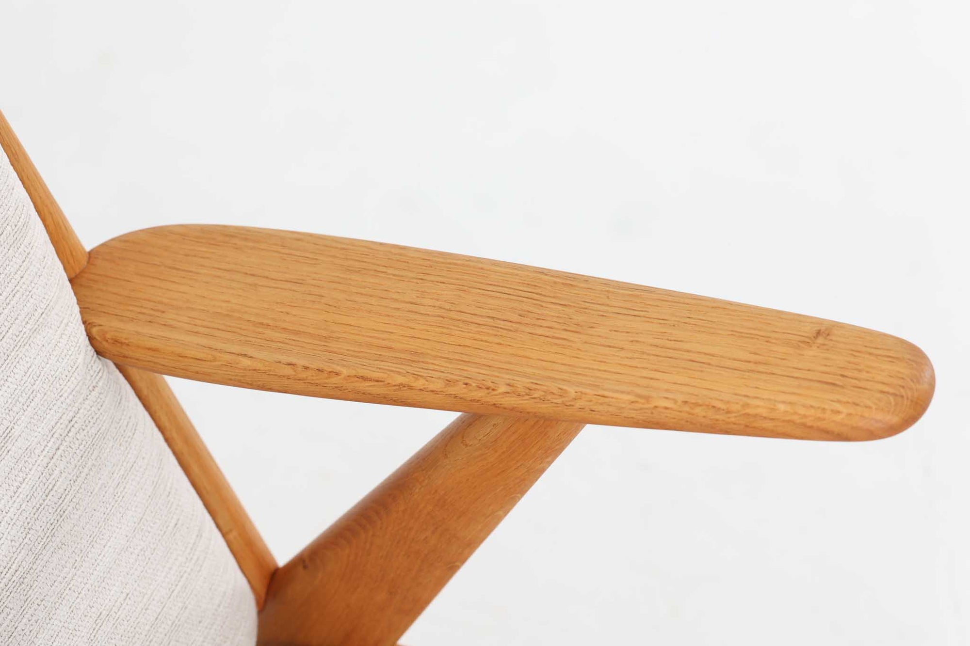 デンマークの国民的ブランドFDBによるビンテージのイージーチェア「J53」。デザイナーは北欧モダンデザインの旗手、Poul m. Volther（ポール・m・ヴォルター）。J53は同氏が手掛けたJシリーズの中でも希少なラウンジチェアタイプで、ゆったりとした座り心地とシンプルな構造美が魅力です。フレームには美しい木目を持つオーク材が使用されており、ナチュラルな風合いが北欧らしい温もりを感じさせます。背面の縦格子デザインや、柔らかくカーブしたアームの形状にも同氏ならではのディテールが感じられます。クッションは新たに張り替え済みで、清潔感のあるアイボリー系のファブリックが品のある印象を与えます。背面に「mADE IN DENmARK」およびFDBの刻印あり。