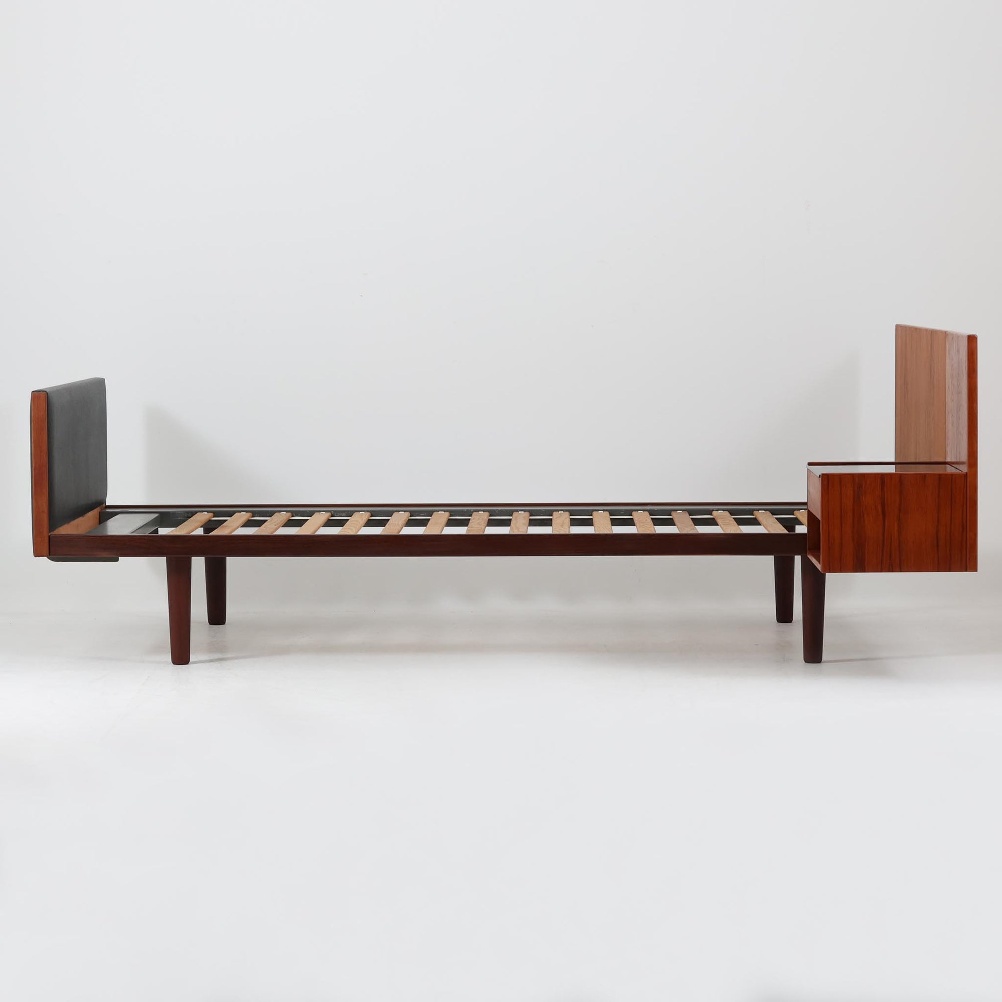 Hans J. Wegnerがデザインし、Getama社によって製造されたこちらのシングルベッドフレームは、チーク材とブラックの合皮パネルが上品に調和した、北欧ビンテージならではの美しい佇まいが魅力です。ヘッドボードにはブラックガラスを載せた引き出し付きのナイトテーブルが備えられていますが、取り外しが可能な構造となっており、空間や用途に応じて柔軟にレイアウトできます。堅牢なスノコ構造で寝具の通気性にも優れ、実用性とデザイン性を兼ね備えた一点です。