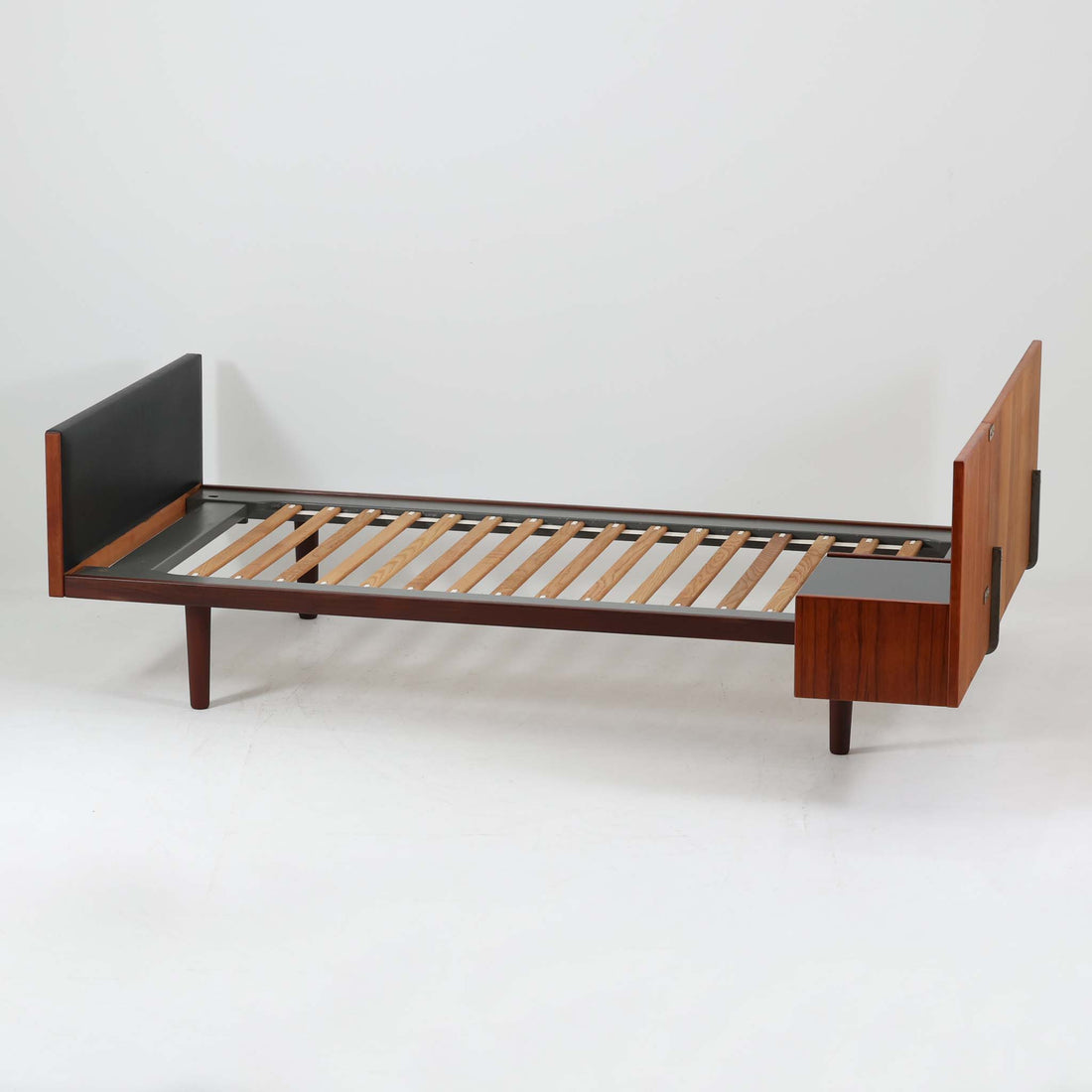 Hans J. Wegnerがデザインし、Getama社によって製造されたこちらのシングルベッドフレームは、チーク材とブラックの合皮パネルが上品に調和した、北欧ビンテージならではの美しい佇まいが魅力です。ヘッドボードにはブラックガラスを載せた引き出し付きのナイトテーブルが備えられていますが、取り外しが可能な構造となっており、空間や用途に応じて柔軟にレイアウトできます。堅牢なスノコ構造で寝具の通気性にも優れ、実用性とデザイン性を兼ね備えた一点です。