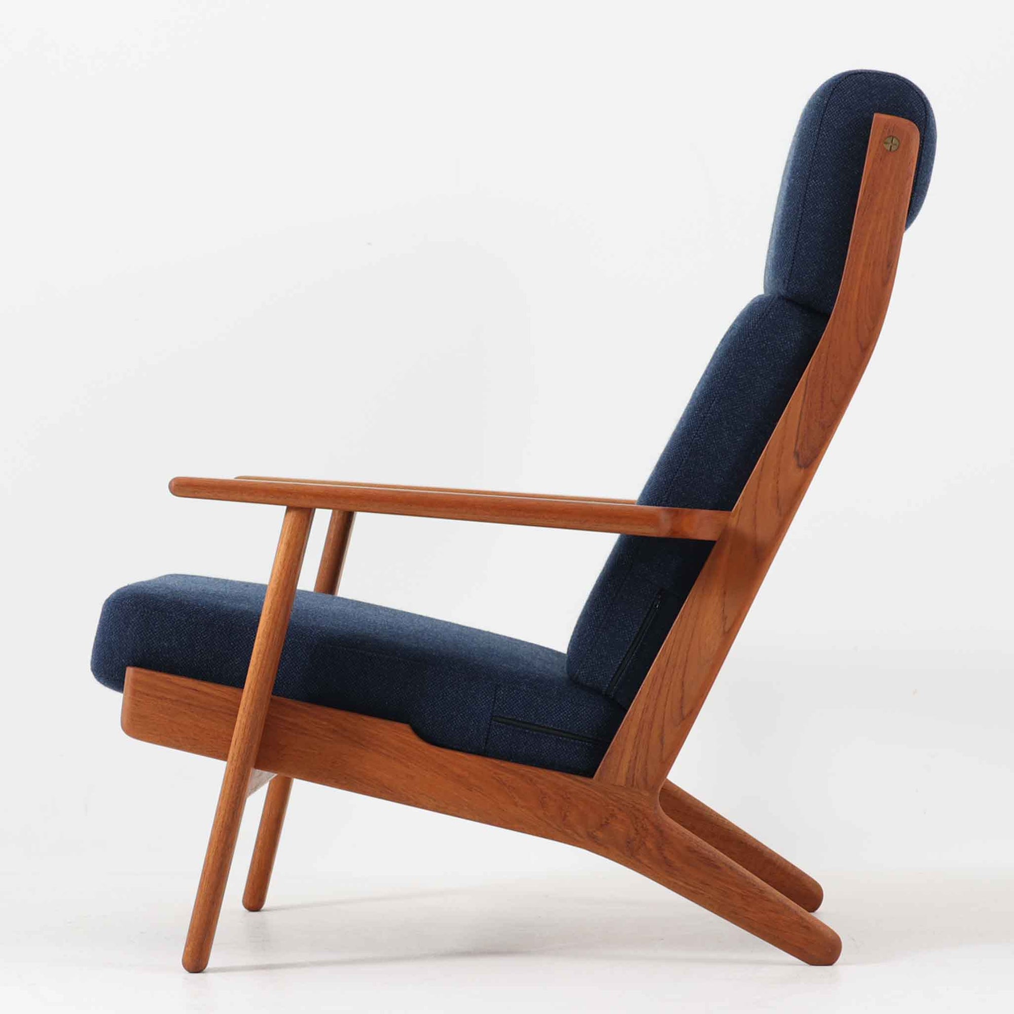 Hans J. Wegnerがデザインし、Getama社によって製造されたGe290Aは、現在では希少となったチーク材のフレームに深いブルーの張地が美しく調和した、ハイバック仕様のビンテージシングルソファです。緩やかに傾斜する背もたれと幅広のアームが身体を包み込むような快適な座り心地を実現し、日常に上質な寛ぎをもたらします。背面の格子状フレームや真鍮ビスなど、細部にまでウェグナーの美意識が宿り、北欧家具の名作としてリビングの主役にふさわしい存在感を放ちます。座面クッションにはスプリングが内包されていますが、背もたれにはウレタンのみが使用されています。