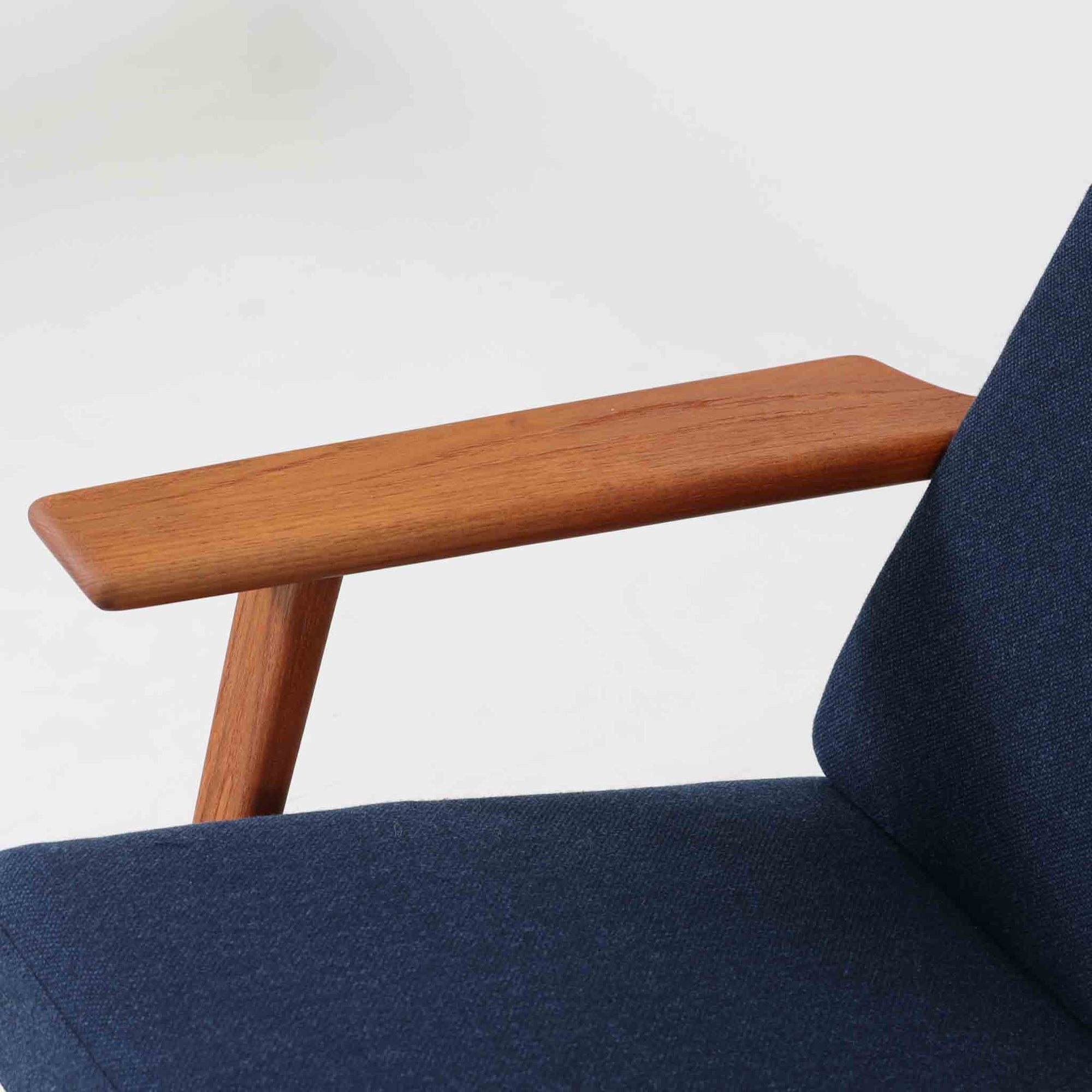Hans J. Wegnerがデザインし、Getama社によって製造されたGe290Aは、現在では希少となったチーク材のフレームに深いブルーの張地が美しく調和した、ハイバック仕様のビンテージシングルソファです。緩やかに傾斜する背もたれと幅広のアームが身体を包み込むような快適な座り心地を実現し、日常に上質な寛ぎをもたらします。背面の格子状フレームや真鍮ビスなど、細部にまでウェグナーの美意識が宿り、北欧家具の名作としてリビングの主役にふさわしい存在感を放ちます。座面クッションにはスプリングが内包されていますが、背もたれにはウレタンのみが使用されています。