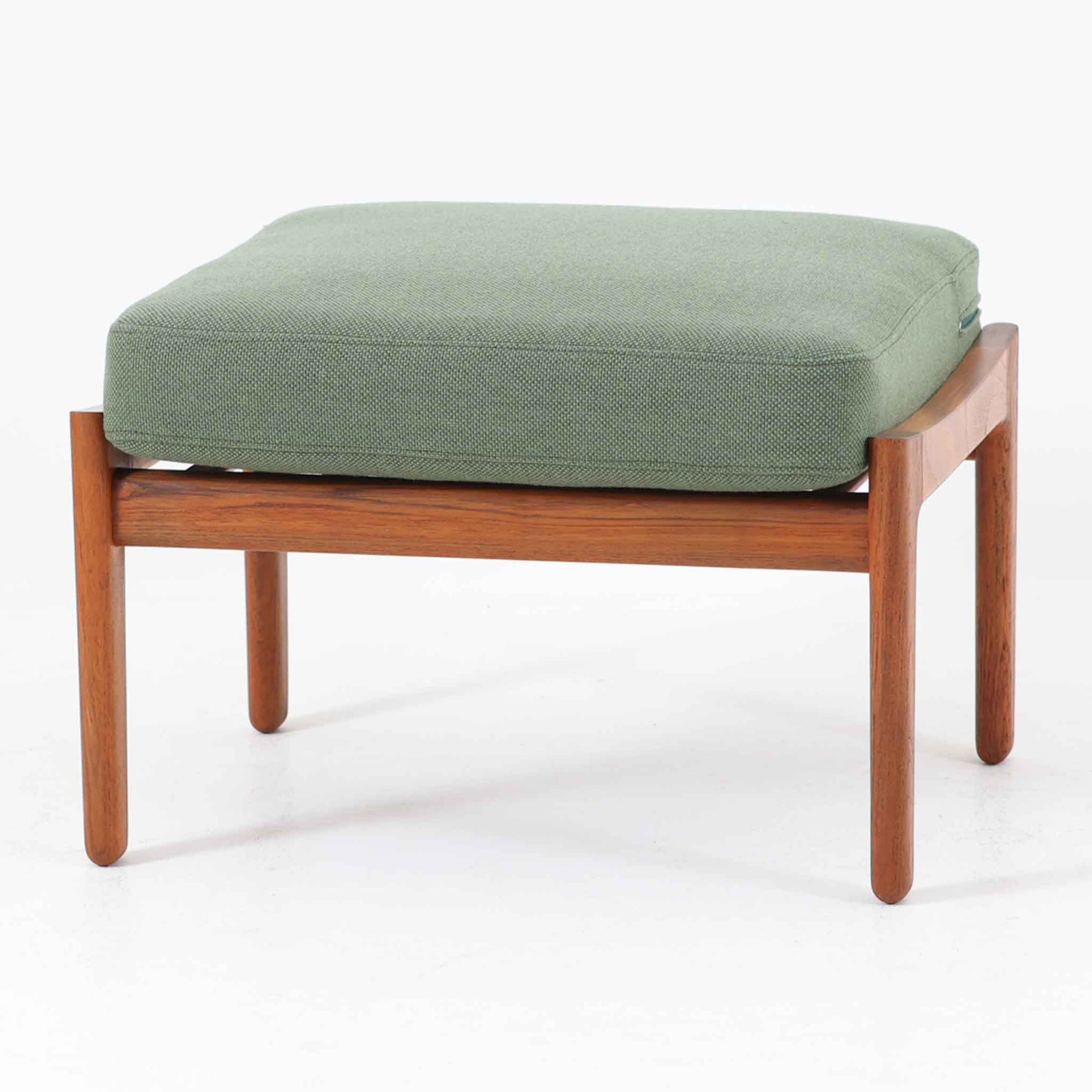 Hans J. Wegnerがデザインし、Getama社によって製造されたGE290オットマンは、堅牢なチーク無垢材のフレームと、美しい格子状のベース構造が特徴の名作です。チーク材仕様のモデルは現存数が少なく、希少価値の高い一台となっています。クッション内部にはスプリングが内包されており、張地にはアクリルとウールを混紡したグリーン系のファブリックが使用され、やわらかな風合いと快適な座り心地を実現。単体でも、同シリーズのソファと組み合わせても使いやすく、北欧ビンテージらしい実用性と美しさを兼ね備えています。