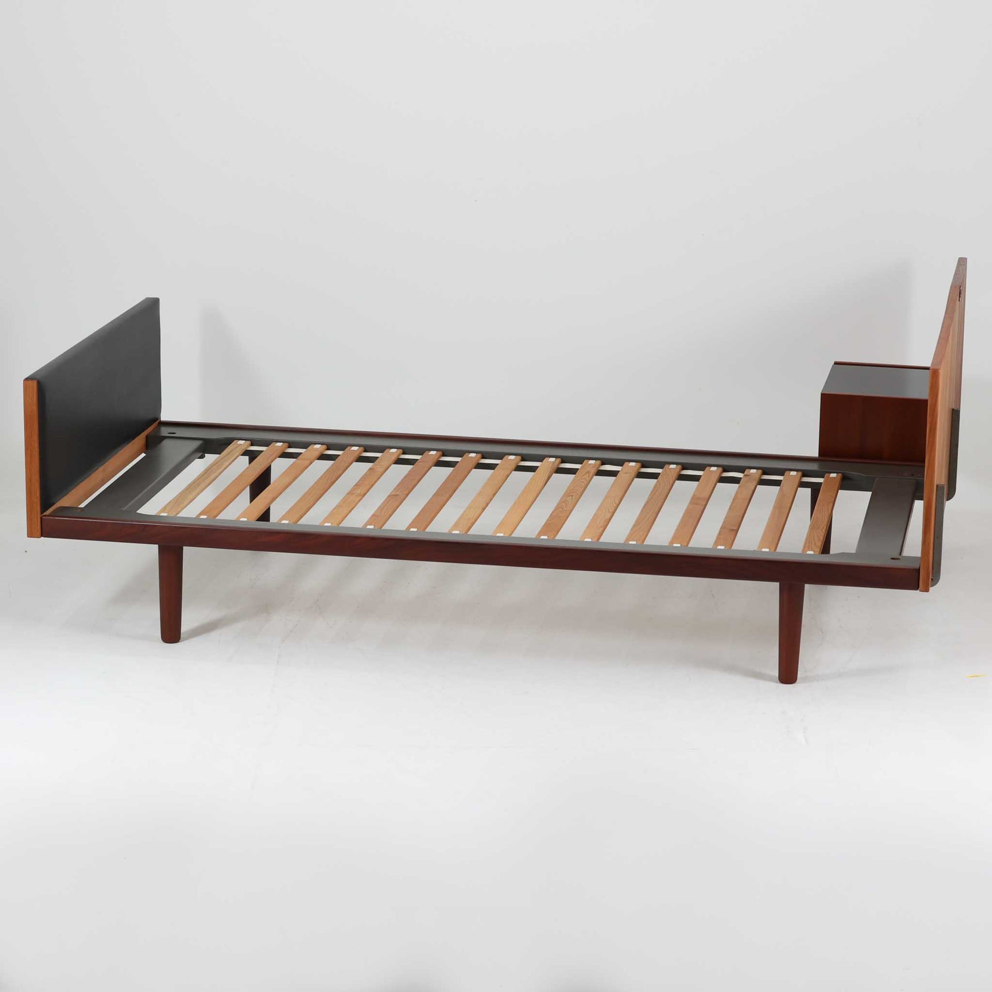 Hans J. Wegnerがデザインし、Getama社によって製造されたこちらのシングルベッドフレームは、チーク材とブラックの合皮パネルが上品に調和した、北欧ビンテージならではの美しい佇まいが魅力です。ヘッドボードにはブラックガラスを載せた引き出し付きのナイトテーブルが備えられていますが、取り外しが可能な構造となっており、空間や用途に応じて柔軟にレイアウトできます。堅牢なスノコ構造で寝具の通気性にも優れ、実用性とデザイン性を兼ね備えた一点です。