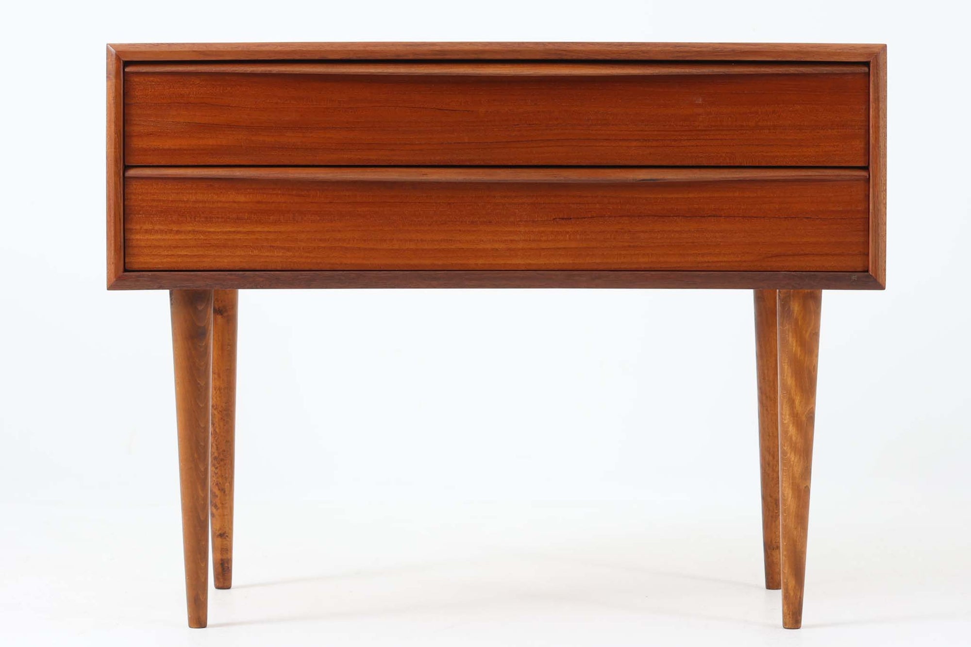 温かみのある木目が魅力的なチーク材を使用した、北欧ビンテージの2段チェストです。直線的なフォルムに、先細りのナチュラルな色味のビーチ材テーパー脚を組み合わせたミニマルなデザインが美しく、空間に軽やかな印象をもたらします。引き出し前板は、手掛けによって開閉できる仕様となっており、すっきりとしたデザイン性と実用性を兼ね備えています。フレーム縁も丁寧に削り出されており、細部までクオリティの高い仕上がりが感じられます。底面には「Jacob Amstrup Funder」の刻印が確認でき、かつてデンマーク・VestbjergにあるRenovere møblerにて丁寧に修復されたことがうかがえます。ベッドサイドやリビングの一角、玄関収納など、さまざまなシーンで活躍する一台です。