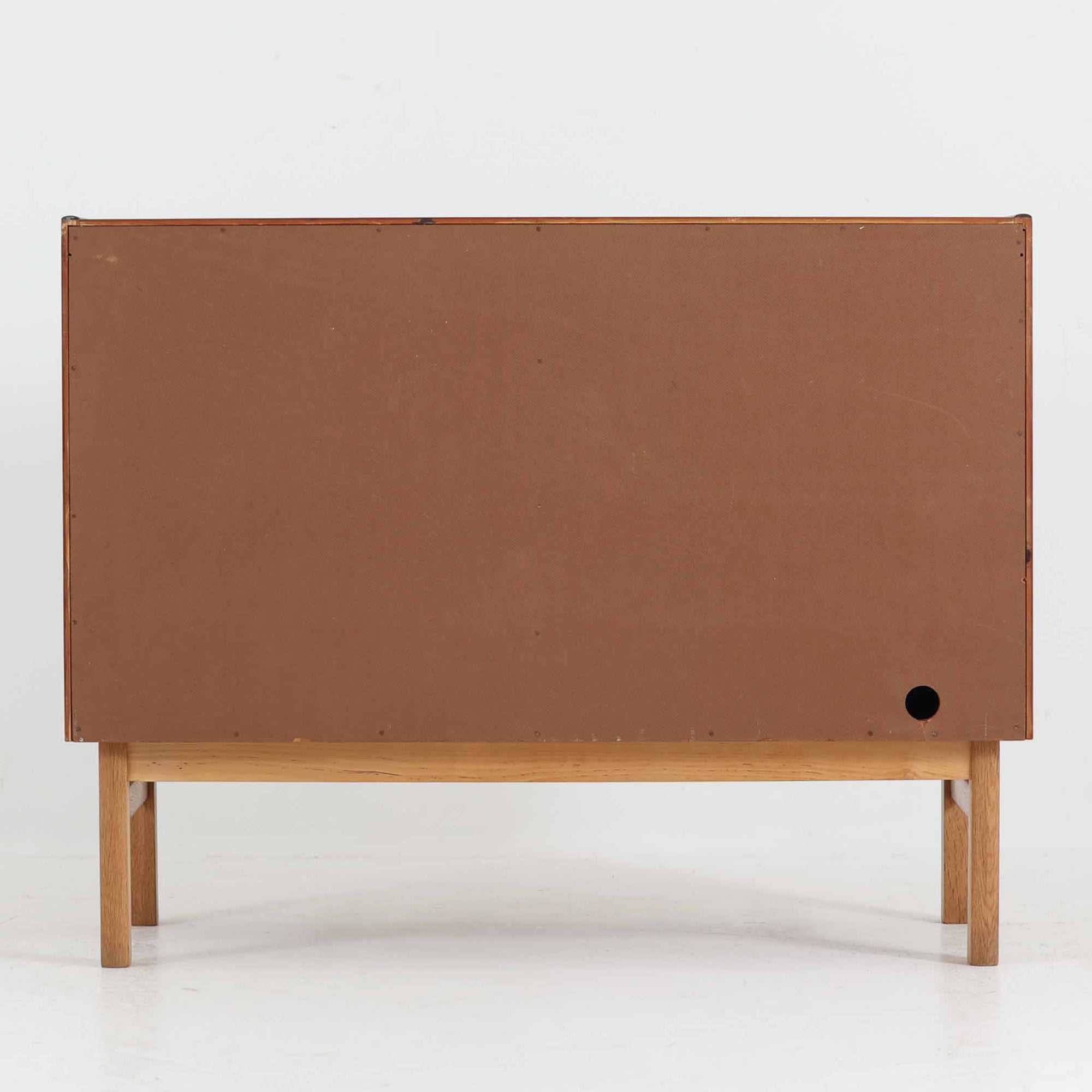 デンマーク製の小ぶりな北欧ビンテージボードで、チーク材とオーク材の組み合わせが上品な一台です。幅90cmとコンパクトながら、引き出し4杯とスライド扉付きの収納部を備え、実用性に優れています。丸いくり抜きの取っ手や直線的な脚部のデザインが軽快な印象を与え、どんな空間にも馴染みやすい造りです。背面の収納部には配線用の穴があり、オーディオや小型テレビ台としても活用可能です。経年により深みを増した木肌が、北欧家具ならではの味わいを感じさせます。