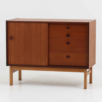 デンマーク製の小ぶりな北欧ビンテージボードで、チーク材とオーク材の組み合わせが上品な一台です。幅90cmとコンパクトながら、引き出し4杯とスライド扉付きの収納部を備え、実用性に優れています。丸いくり抜きの取っ手や直線的な脚部のデザインが軽快な印象を与え、どんな空間にも馴染みやすい造りです。背面の収納部には配線用の穴があり、オーディオや小型テレビ台としても活用可能です。経年により深みを増した木肌が、北欧家具ならではの味わいを感じさせます。