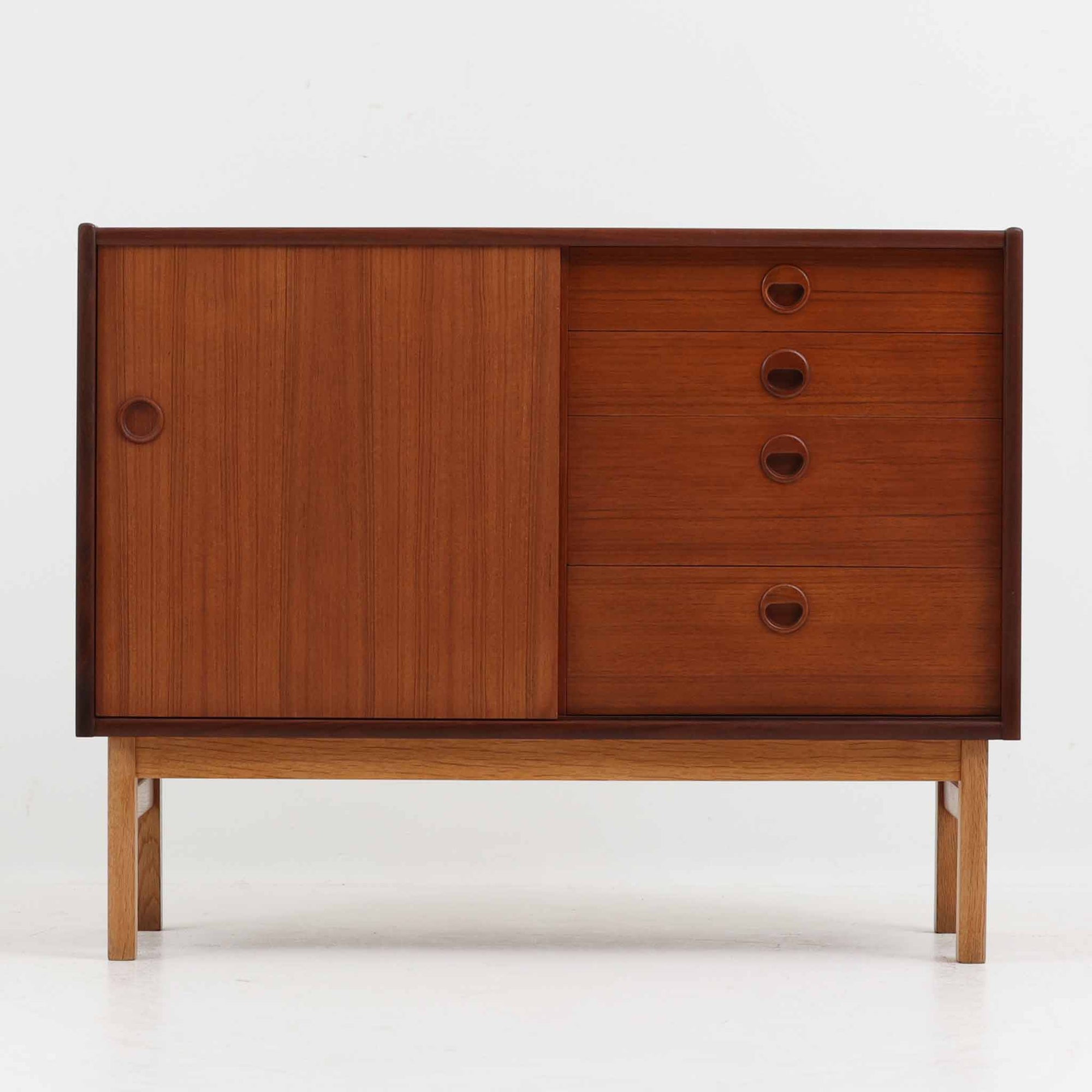 デンマーク製の小ぶりな北欧ビンテージボードで、チーク材とオーク材の組み合わせが上品な一台です。幅90cmとコンパクトながら、引き出し4杯とスライド扉付きの収納部を備え、実用性に優れています。丸いくり抜きの取っ手や直線的な脚部のデザインが軽快な印象を与え、どんな空間にも馴染みやすい造りです。背面の収納部には配線用の穴があり、オーディオや小型テレビ台としても活用可能です。経年により深みを増した木肌が、北欧家具ならではの味わいを感じさせます。