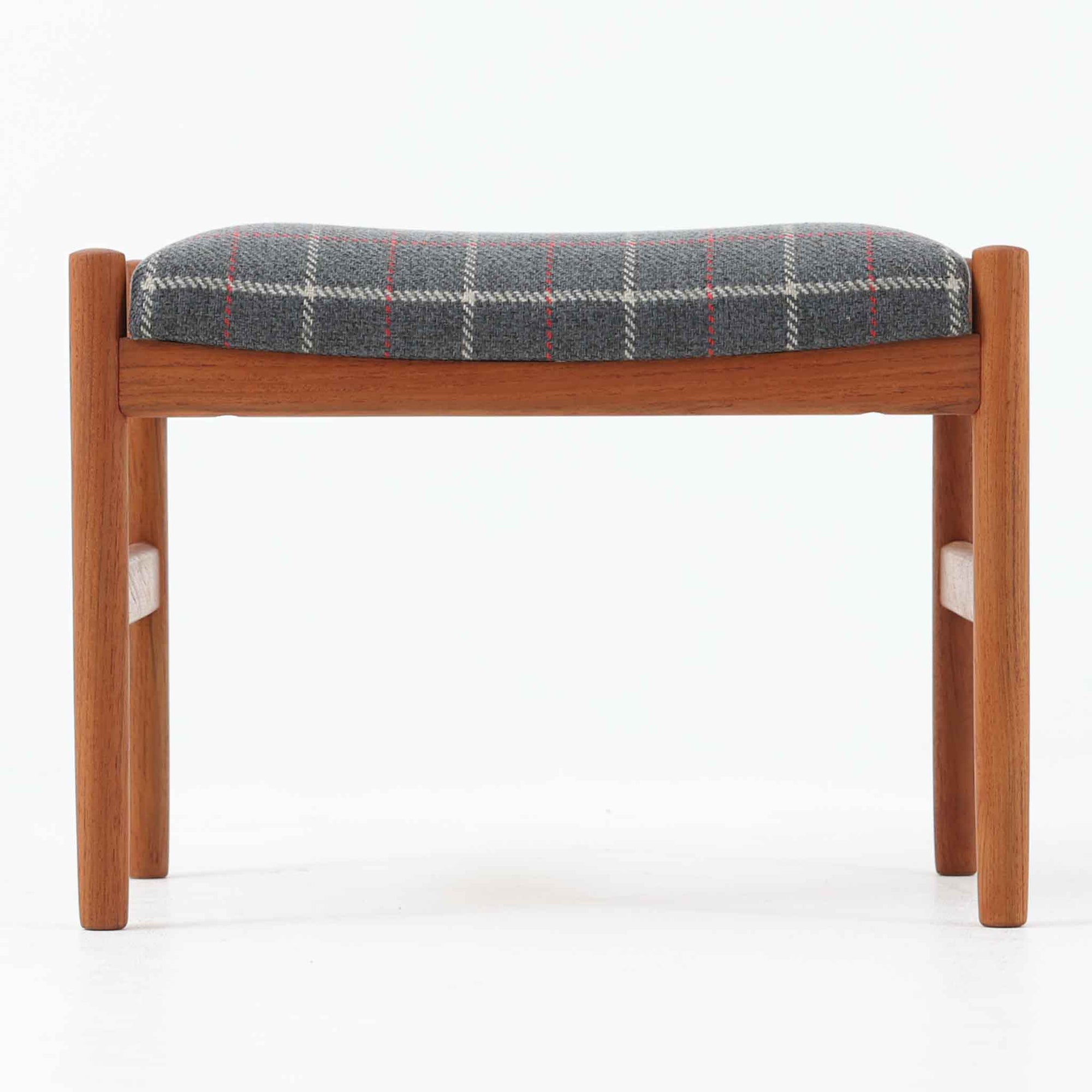 デンマーク製のこちらのスツールは、チーク材の温かみあるフレームに、日本メーカーのチェック柄ファブリックで張り替えを施した、北欧ビンテージ家具らしい洗練と実用性を兼ね備えた一脚です。脚部は丸棒を用いたシンプルな構造で、細部まで丁寧に仕上げられており、軽やかな佇まいの中に確かな安定感が感じられます。張地にはグレーベースに赤のラインがアクセントとなったチェック柄を採用し、空間に個性と落ち着きをもたらします。玄関やベッドサイド、オットマンとしての使用など幅広い用途に対応できるコンパクトなサイズ感も魅力です。また、裏面には「Danish Furnituremakers Control」ラベルが残されており、品質の高さを証明する一品です。経年により深まった木部の風合いと張地のコンビネーションが美しいスツールです。
