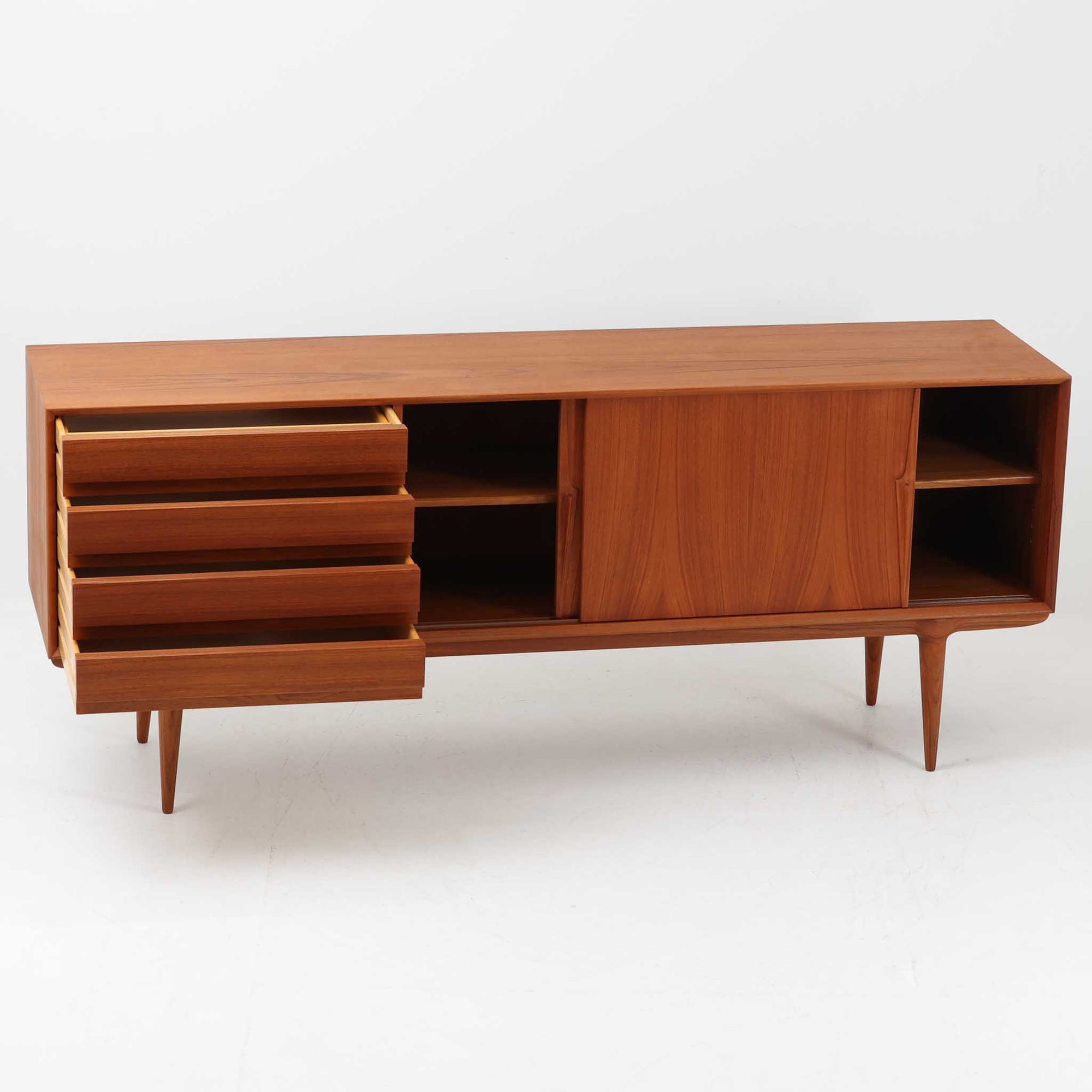 Gunni Omannがデザインし、Omann Jun社によって製造されたModel 18は、洗練されたラインと実用性を兼ね備えた北欧ビンテージの名作サイドボードです。チーク材の美しい木目が前面に広がり、引き出しとスライド扉の組み合わせが高い収納力を実現しています。特に繊細に削り出された取手や先細りの脚部が、軽やかで彫刻的な印象を与え、空間を上質に演出します。幅200cmのサイズ感は、リビングやダイニングの主役として活躍する存在感ある一台です。