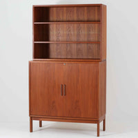 Bjerringbro Savvaerkによるチーク材キャビネットは、上下に分かれた構成と可動棚を備えた収納力の高さが魅力です。上段は3段のシェルフ、下段は珍しいポケットドア構造の扉内にA4サイズの書類が収納可能な引き出し型トレイが8段並び、書類や小物の整理に適しています。直線的で端正なフォルムと、チーク材の木目が美しく調和した佇まいは、北欧ビンテージらしい実用性と美しさを兼ね備えた逸品です。