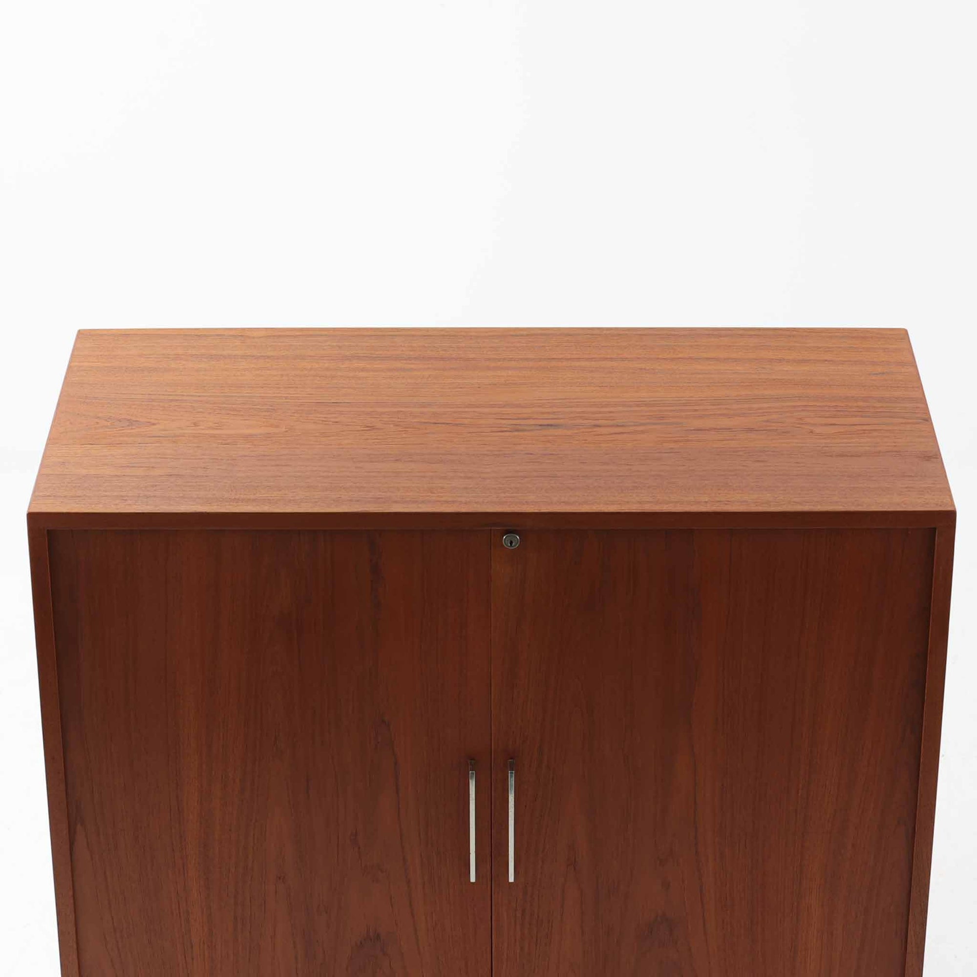 Bjerringbro Savvaerkによるチーク材キャビネットは、上下に分かれた構成と可動棚を備えた収納力の高さが魅力です。上段は3段のシェルフ、下段は珍しいポケットドア構造の扉内にA4サイズの書類が収納可能な引き出し型トレイが8段並び、書類や小物の整理に適しています。直線的で端正なフォルムと、チーク材の木目が美しく調和した佇まいは、北欧ビンテージらしい実用性と美しさを兼ね備えた逸品です。