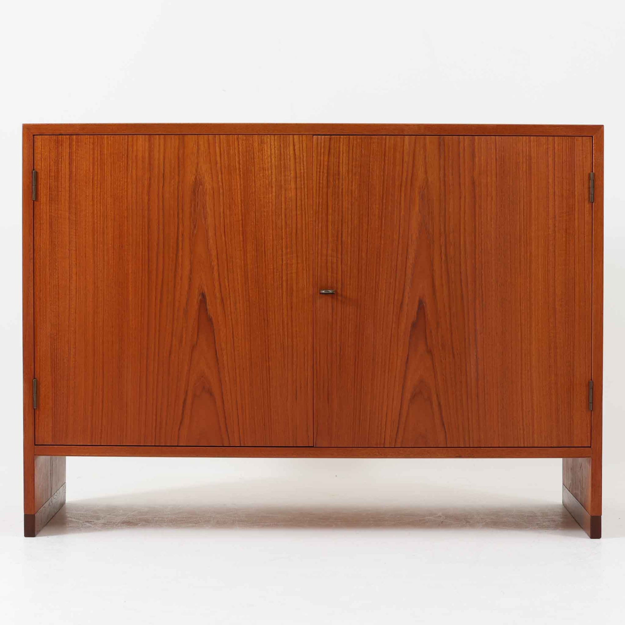 Hans J. Wegner（ハンス・J・ウェグナー）によってデザインされ、RY Mobler社により製造されたこちらのキャビネットは、美しいチーク材と実用的な構造が融合した北欧ビンテージ家具の名作です。扉にはチーク材特有の深い木目が活かされ、中央の控えめな金属製ハンドルがアクセントとなっています。内部は可動棚付きの2室構成で、食器類や書類、小物の整理にも適した収納力を備えています。注目すべきは、足摺にあたる下部のパーツにオーク材が使用されている点で、異なる木材の組み合わせが上質なコントラストを生み出しています。背面には「RY」ロゴと「27 APR 1959」のスタンプが残っており、当時のオリジナルであることが確認できます。リビングやダイニング、書斎などさまざまな空間で、温もりと凛とした佇まいを演出してくれる北欧ビンテージ家具らしい一台です。