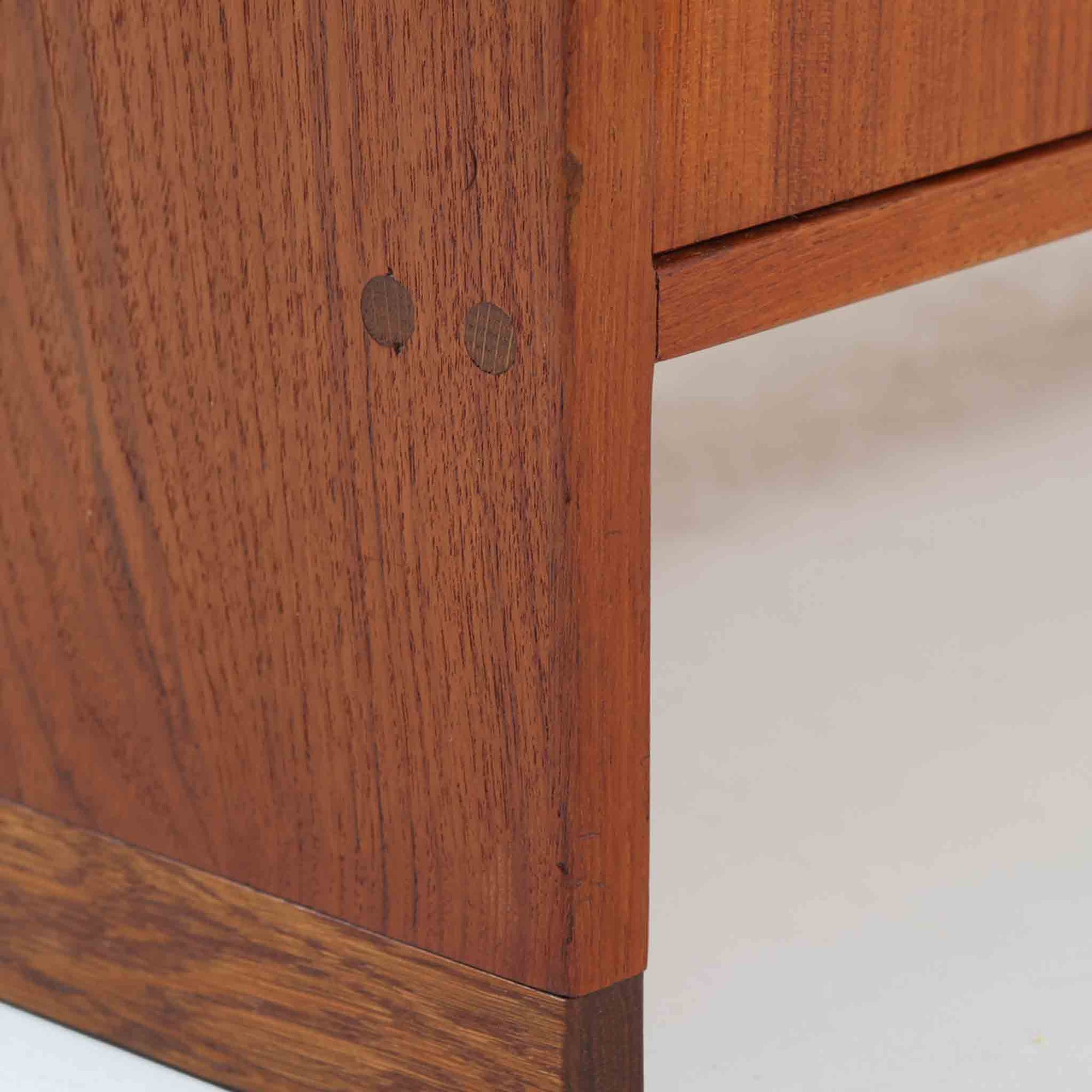 Hans J. Wegner（ハンス・J・ウェグナー）によってデザインされ、RY Mobler社により製造されたこちらのキャビネットは、美しいチーク材と実用的な構造が融合した北欧ビンテージ家具の名作です。扉にはチーク材特有の深い木目が活かされ、中央の控えめな金属製ハンドルがアクセントとなっています。内部は可動棚付きの2室構成で、食器類や書類、小物の整理にも適した収納力を備えています。注目すべきは、足摺にあたる下部のパーツにオーク材が使用されている点で、異なる木材の組み合わせが上質なコントラストを生み出しています。背面には「RY」ロゴと「27 APR 1959」のスタンプが残っており、当時のオリジナルであることが確認できます。リビングやダイニング、書斎などさまざまな空間で、温もりと凛とした佇まいを演出してくれる北欧ビンテージ家具らしい一台です。