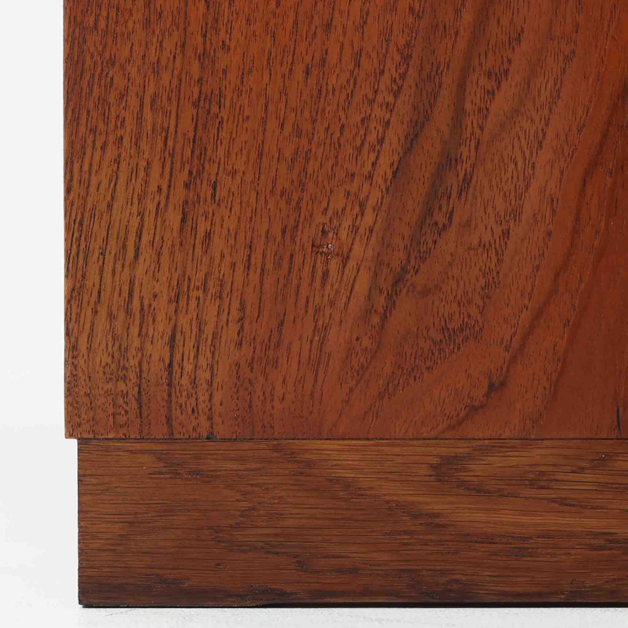 Hans J. Wegner（ハンス・J・ウェグナー）によってデザインされ、RY Mobler社により製造されたこちらのキャビネットは、美しいチーク材と実用的な構造が融合した北欧ビンテージ家具の名作です。扉にはチーク材特有の深い木目が活かされ、中央の控えめな金属製ハンドルがアクセントとなっています。内部は可動棚付きの2室構成で、食器類や書類、小物の整理にも適した収納力を備えています。注目すべきは、足摺にあたる下部のパーツにオーク材が使用されている点で、異なる木材の組み合わせが上質なコントラストを生み出しています。背面には「RY」ロゴと「27 APR 1959」のスタンプが残っており、当時のオリジナルであることが確認できます。リビングやダイニング、書斎などさまざまな空間で、温もりと凛とした佇まいを演出してくれる北欧ビンテージ家具らしい一台です。