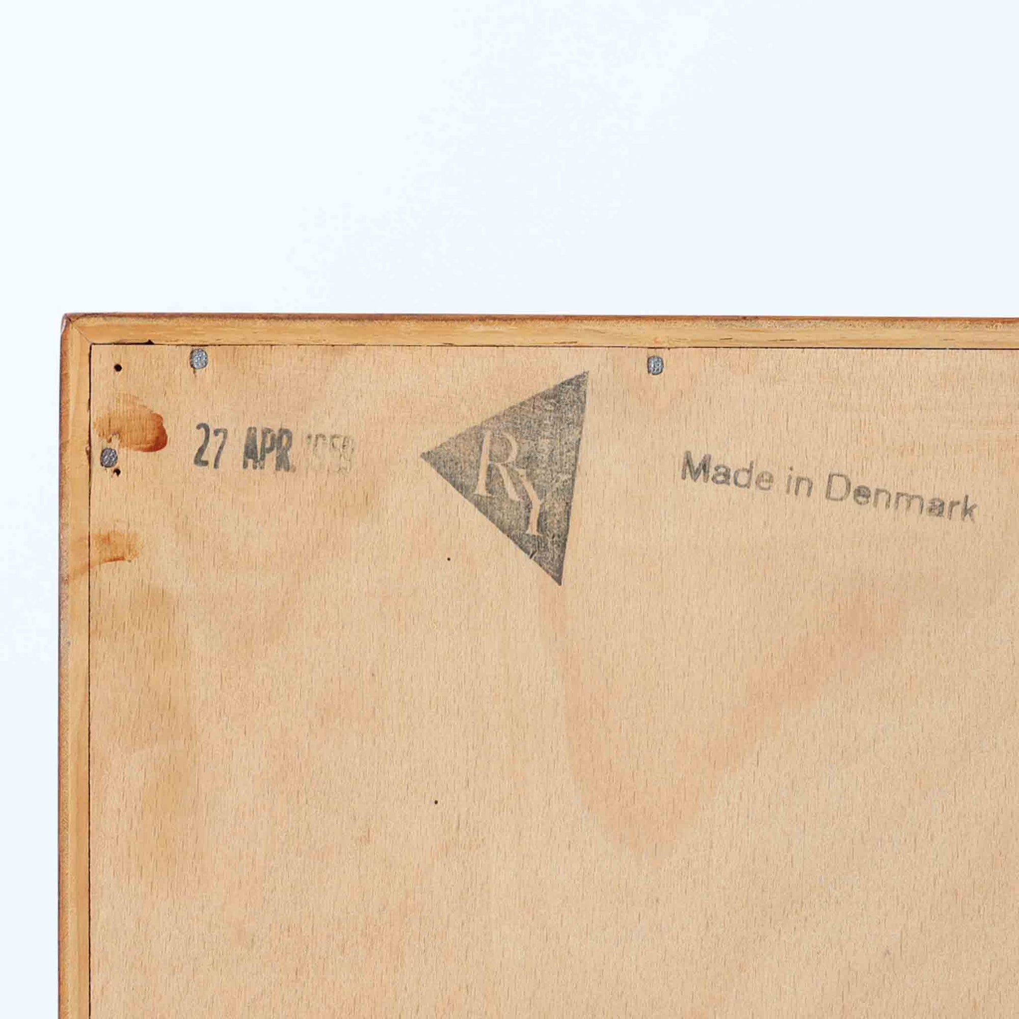 Hans J. Wegner（ハンス・J・ウェグナー）によってデザインされ、RY Mobler社により製造されたこちらのキャビネットは、美しいチーク材と実用的な構造が融合した北欧ビンテージ家具の名作です。扉にはチーク材特有の深い木目が活かされ、中央の控えめな金属製ハンドルがアクセントとなっています。内部は可動棚付きの2室構成で、食器類や書類、小物の整理にも適した収納力を備えています。注目すべきは、足摺にあたる下部のパーツにオーク材が使用されている点で、異なる木材の組み合わせが上質なコントラストを生み出しています。背面には「RY」ロゴと「27 APR 1959」のスタンプが残っており、当時のオリジナルであることが確認できます。リビングやダイニング、書斎などさまざまな空間で、温もりと凛とした佇まいを演出してくれる北欧ビンテージ家具らしい一台です。