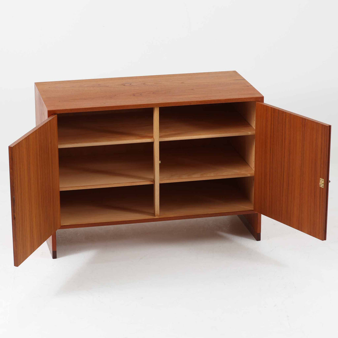 Hans J. Wegner（ハンス・J・ウェグナー）によってデザインされ、RY Mobler社により製造されたこちらのキャビネットは、美しいチーク材と実用的な構造が融合した北欧ビンテージ家具の名作です。扉にはチーク材特有の深い木目が活かされ、中央の控えめな金属製ハンドルがアクセントとなっています。内部は可動棚付きの2室構成で、食器類や書類、小物の整理にも適した収納力を備えています。注目すべきは、足摺にあたる下部のパーツにオーク材が使用されている点で、異なる木材の組み合わせが上質なコントラストを生み出しています。背面には「RY」ロゴと「27 APR 1959」のスタンプが残っており、当時のオリジナルであることが確認できます。リビングやダイニング、書斎などさまざまな空間で、温もりと凛とした佇まいを演出してくれる北欧ビンテージ家具らしい一台です。