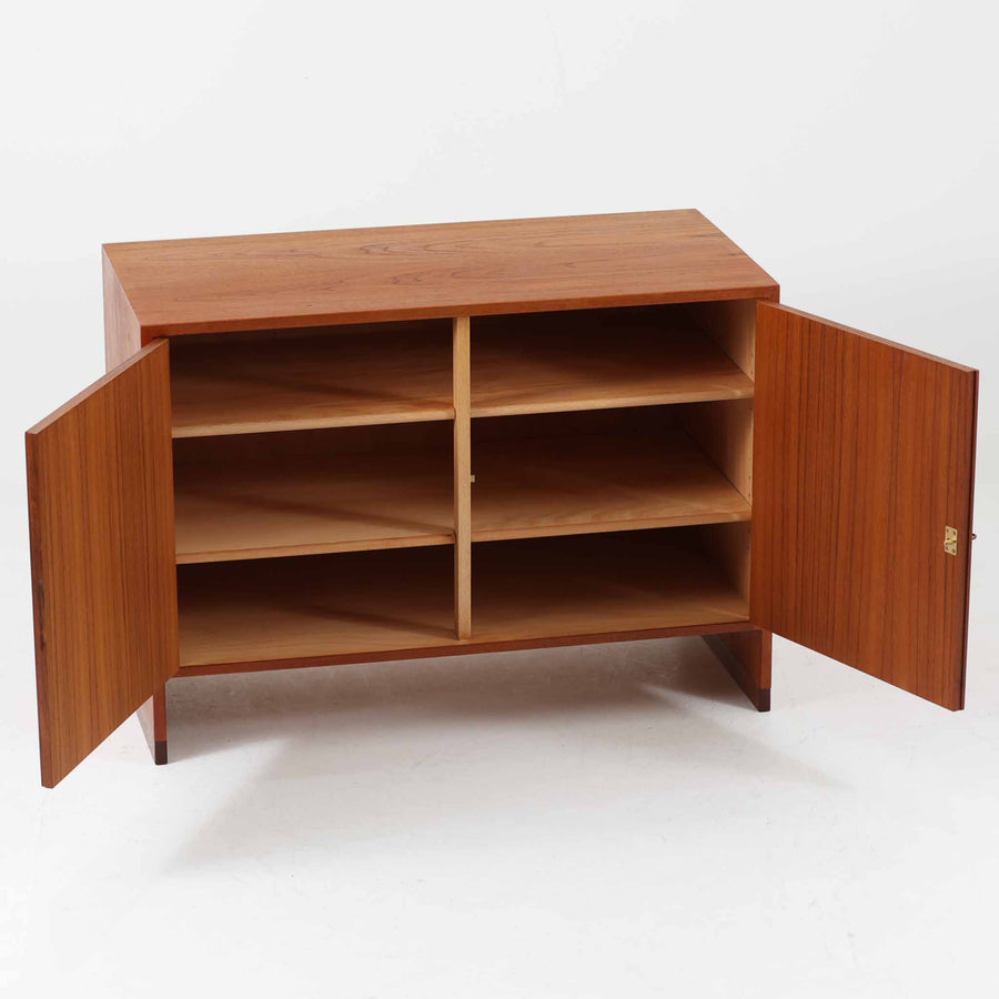 Hans J. Wegner（ハンス・J・ウェグナー）によってデザインされ、RY Mobler社により製造されたこちらのキャビネットは、美しいチーク材と実用的な構造が融合した北欧ビンテージ家具の名作です。扉にはチーク材特有の深い木目が活かされ、中央の控えめな金属製ハンドルがアクセントとなっています。内部は可動棚付きの2室構成で、食器類や書類、小物の整理にも適した収納力を備えています。注目すべきは、足摺にあたる下部のパーツにオーク材が使用されている点で、異なる木材の組み合わせが上質なコントラストを生み出しています。背面には「RY」ロゴと「27 APR 1959」のスタンプが残っており、当時のオリジナルであることが確認できます。リビングやダイニング、書斎などさまざまな空間で、温もりと凛とした佇まいを演出してくれる北欧ビンテージ家具らしい一台です。
