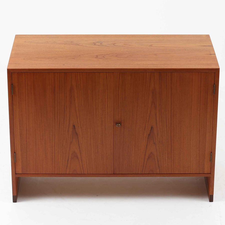 Hans J. Wegner（ハンス・J・ウェグナー）によってデザインされ、RY Mobler社により製造されたこちらのキャビネットは、美しいチーク材と実用的な構造が融合した北欧ビンテージ家具の名作です。扉にはチーク材特有の深い木目が活かされ、中央の控えめな金属製ハンドルがアクセントとなっています。内部は可動棚付きの2室構成で、食器類や書類、小物の整理にも適した収納力を備えています。注目すべきは、足摺にあたる下部のパーツにオーク材が使用されている点で、異なる木材の組み合わせが上質なコントラストを生み出しています。背面には「RY」ロゴと「27 APR 1959」のスタンプが残っており、当時のオリジナルであることが確認できます。リビングやダイニング、書斎などさまざまな空間で、温もりと凛とした佇まいを演出してくれる北欧ビンテージ家具らしい一台です。