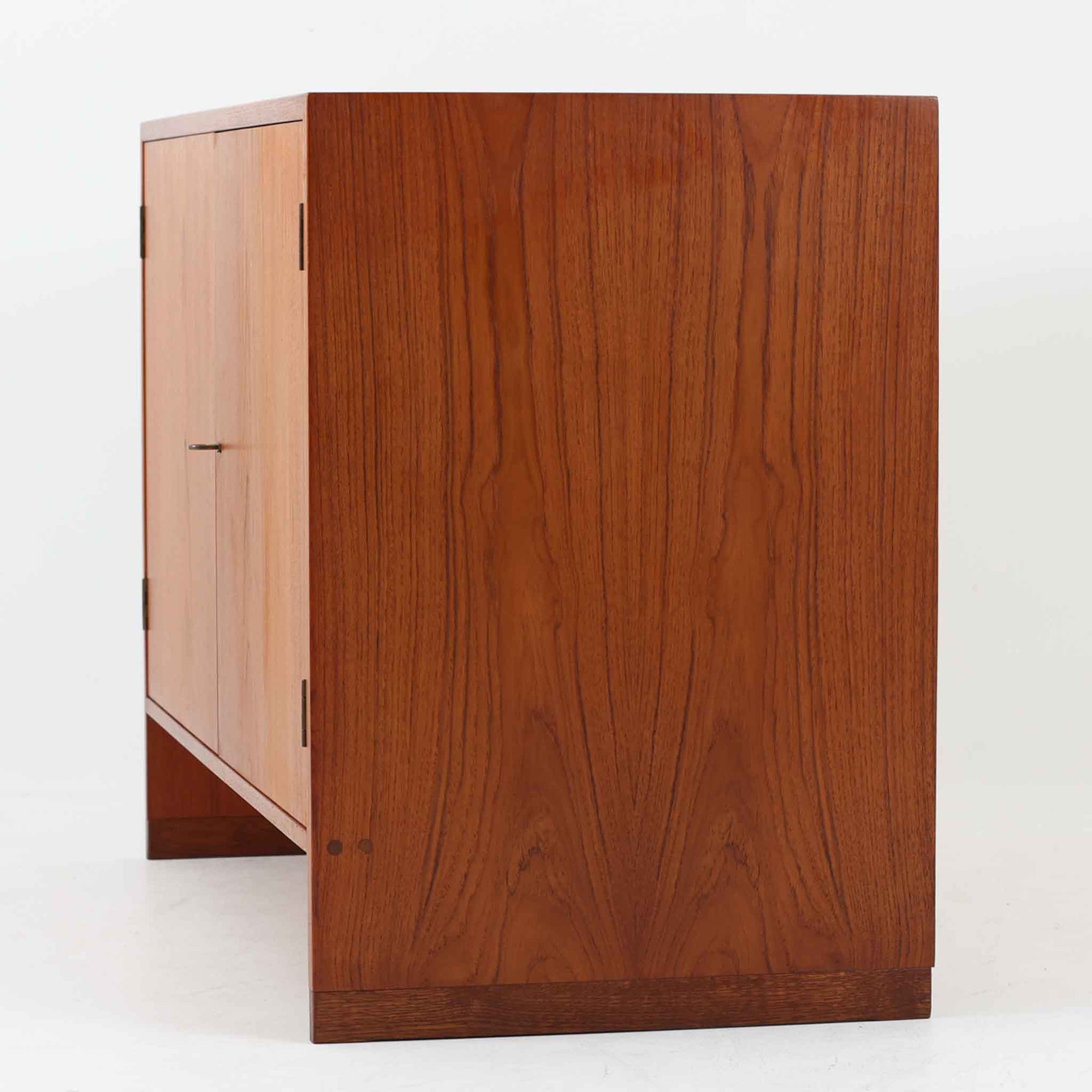 Hans J. Wegner（ハンス・J・ウェグナー）によってデザインされ、RY Mobler社により製造されたこちらのキャビネットは、美しいチーク材と実用的な構造が融合した北欧ビンテージ家具の名作です。扉にはチーク材特有の深い木目が活かされ、中央の控えめな金属製ハンドルがアクセントとなっています。内部は可動棚付きの2室構成で、食器類や書類、小物の整理にも適した収納力を備えています。注目すべきは、足摺にあたる下部のパーツにオーク材が使用されている点で、異なる木材の組み合わせが上質なコントラストを生み出しています。背面には「RY」ロゴと「27 APR 1959」のスタンプが残っており、当時のオリジナルであることが確認できます。リビングやダイニング、書斎などさまざまな空間で、温もりと凛とした佇まいを演出してくれる北欧ビンテージ家具らしい一台です。