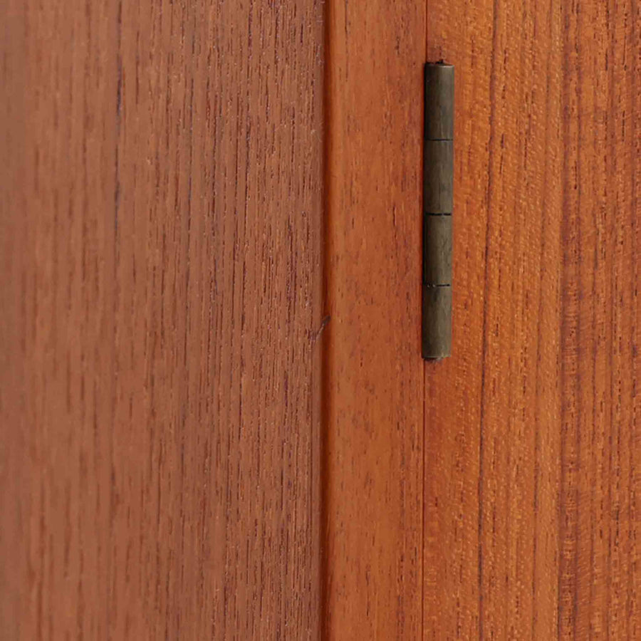 Hans J. Wegner（ハンス・J・ウェグナー）によってデザインされ、RY Mobler社により製造されたこちらのキャビネットは、美しいチーク材と実用的な構造が融合した北欧ビンテージ家具の名作です。扉にはチーク材特有の深い木目が活かされ、中央の控えめな金属製ハンドルがアクセントとなっています。内部は可動棚付きの2室構成で、食器類や書類、小物の整理にも適した収納力を備えています。注目すべきは、足摺にあたる下部のパーツにオーク材が使用されている点で、異なる木材の組み合わせが上質なコントラストを生み出しています。背面には「RY」ロゴと「27 APR 1959」のスタンプが残っており、当時のオリジナルであることが確認できます。リビングやダイニング、書斎などさまざまな空間で、温もりと凛とした佇まいを演出してくれる北欧ビンテージ家具らしい一台です。